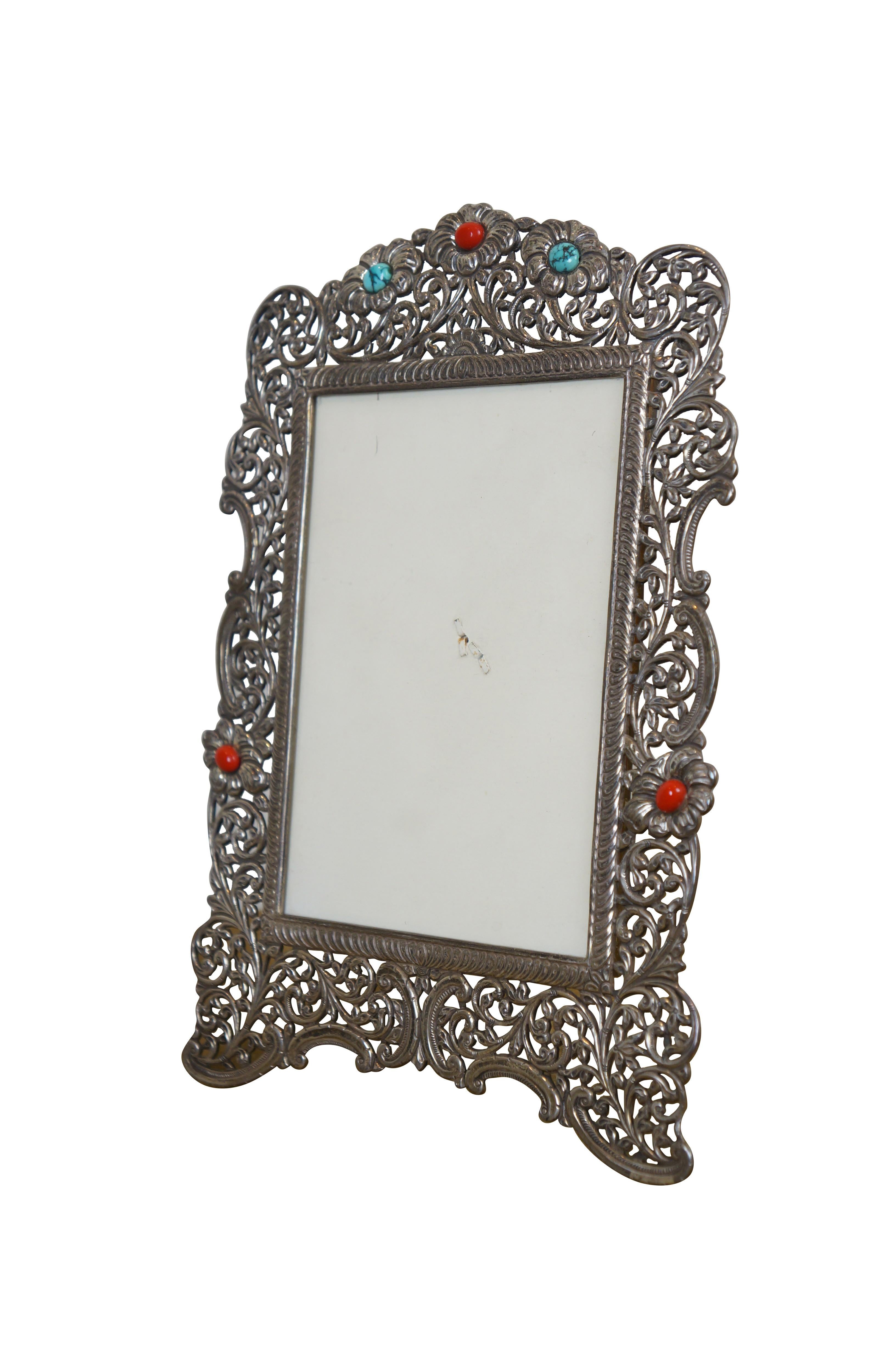 Cornice rettangolare verticale in argento sterling 925 in stile art nouveau con filigrana floreale e fogliare traforata, arricchita da pietre rosso corallo e turchese venato. Retro del cavalletto. 

Dimensioni:
8.5