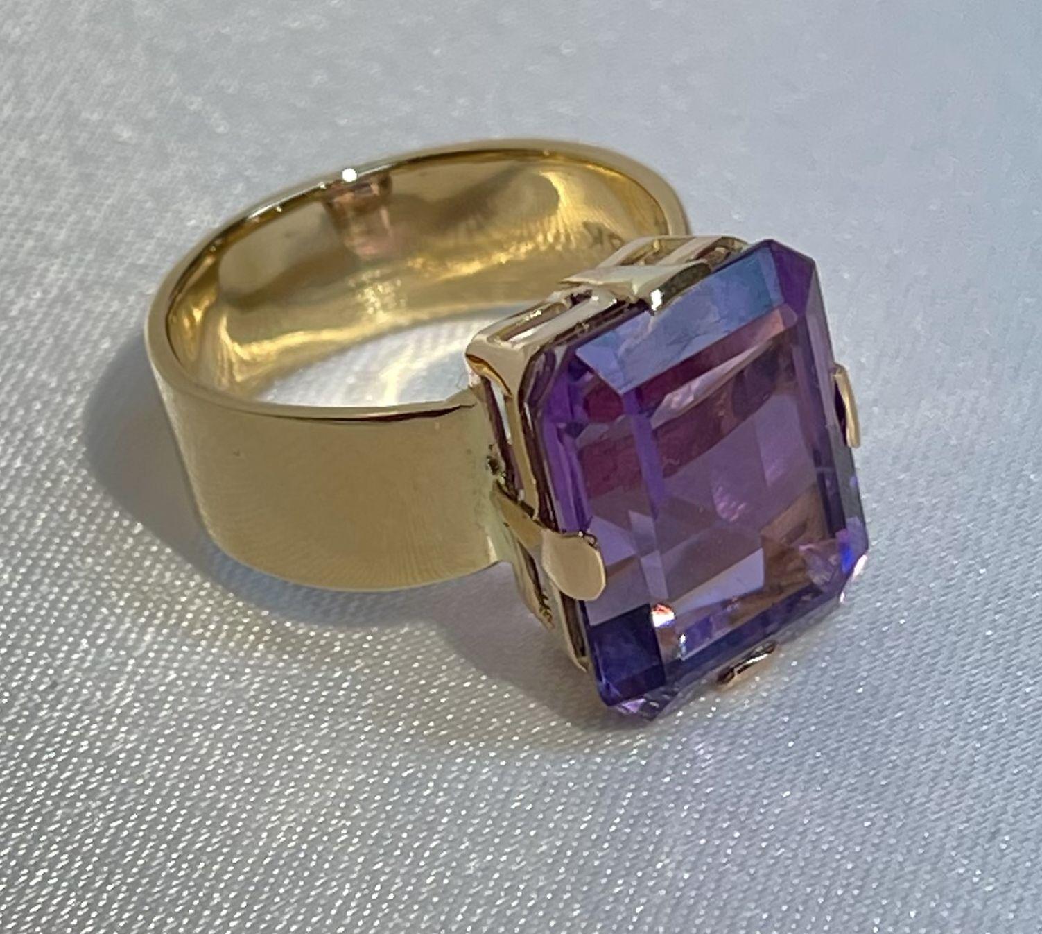Simply Beautiful! Finely detailed Statement Large Emerald Cut Amethyst Solitaire Gold Cocktail Ring. Centering a securely nestled 9.60 Carat Emerald-cut Amethyst in prong setting. Amethyst measures approx. 14.3mm l x 11.8mm w x 8.5mm d. Hand crafted