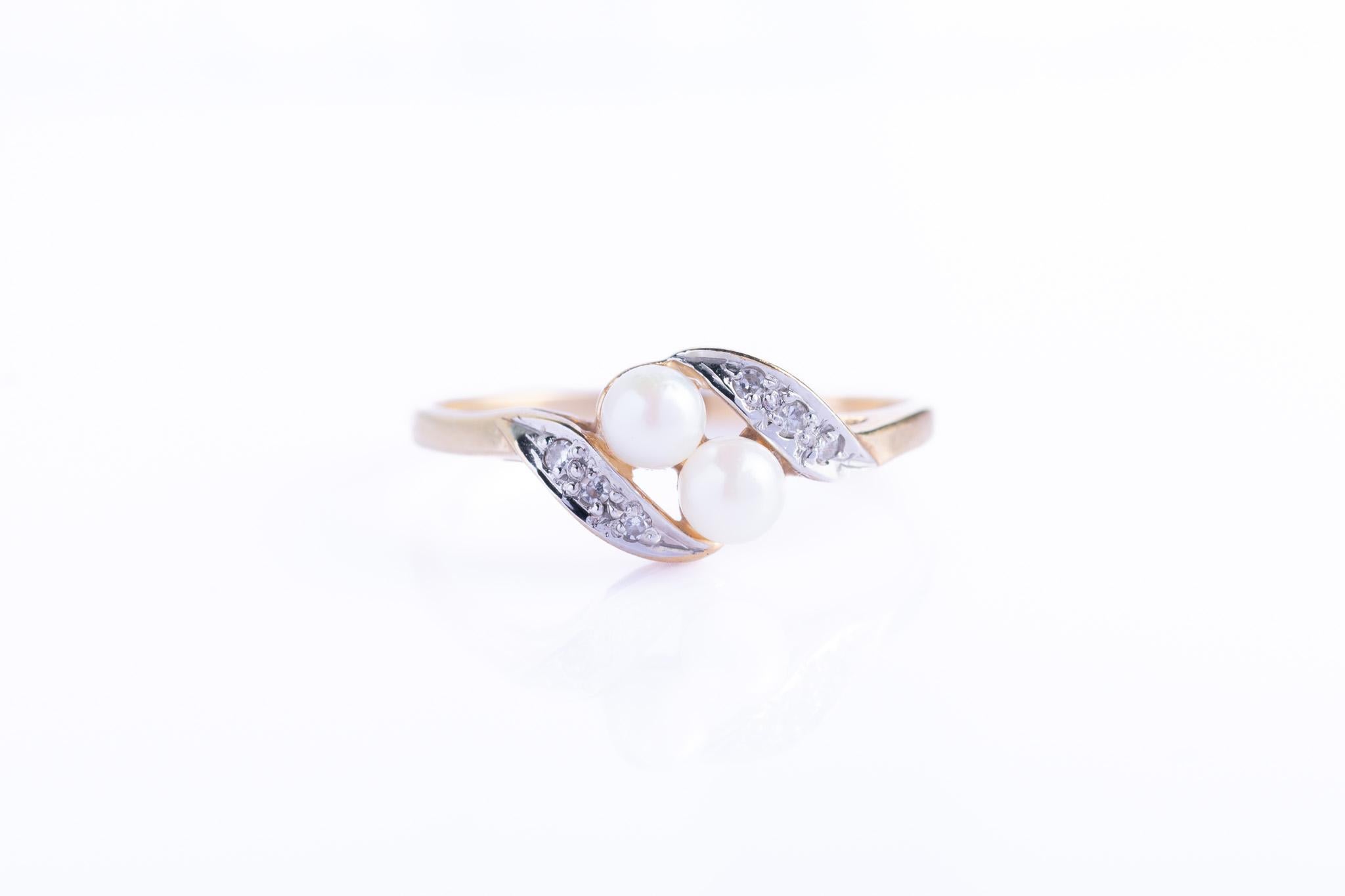 An elegant crossover ring in 9ct gold, set with two creamy pearls at its centre, a classic toi et moi design, symbolising “you and me.” The pearls are framed by gentle sweeps of white gold, each set with sparkling diamonds that catch the light with