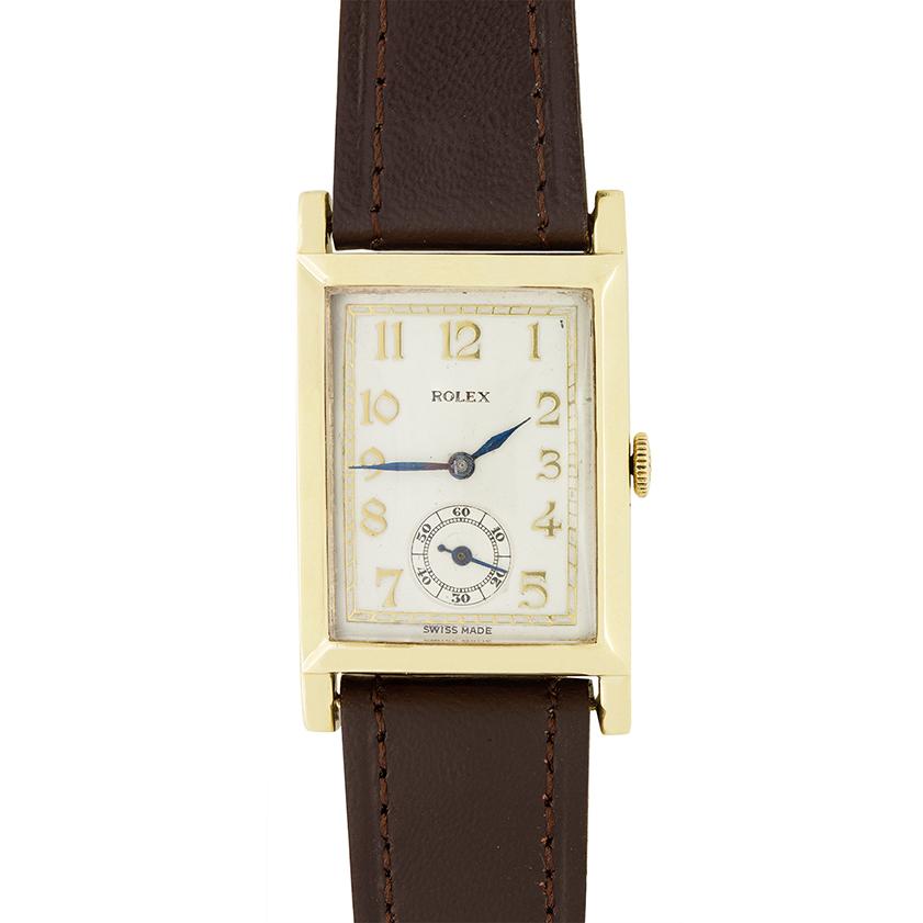 De los años 40 es este precioso reloj Rolex La caja de oro amarillo de 9 quilates tiene forma rectangular y mide 24 mm por 39 mm. Un movimiento de cuerda manual constituye el corazón del reloj. Los números arábigos marcan las horas, con el logotipo