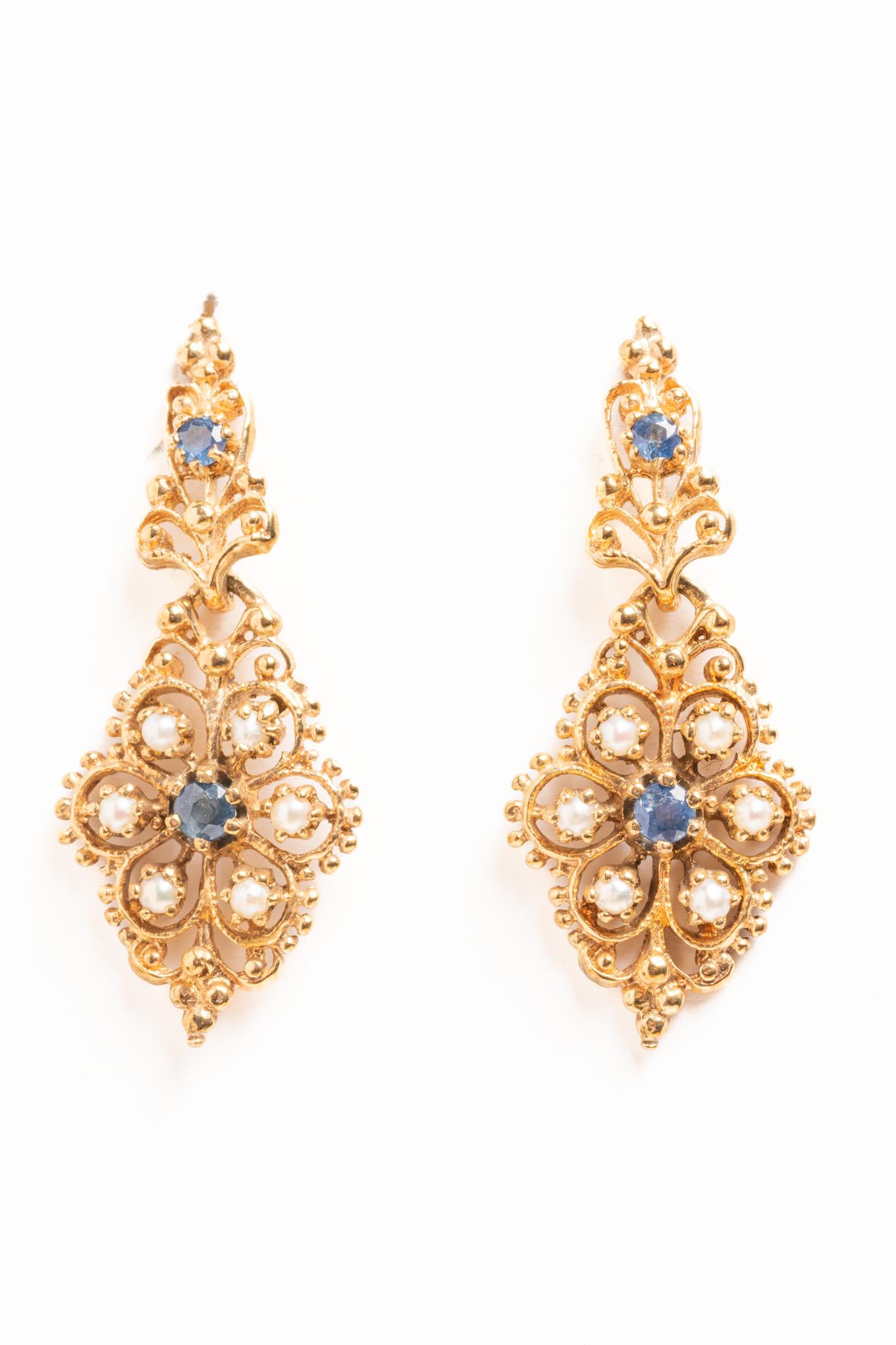 A spectacular pair of vintage Victorian style ornate drop earrings adorned with blue sapphires and beautiful seed pearls. Each earring is decorated with two sapphires and six seed pearls designed in a form of a daisy flower, crowned with a tiny