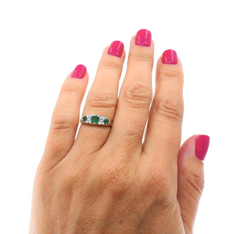 Questo elegante anello vintage è realizzato in oro 9 carati (marchio 375) e incastonato con tre smeraldi di taglio rotondo sul davanti, accentati da piccoli diamanti per una sottile brillantezza. Lo smeraldo centrale è leggermente più grande ed è