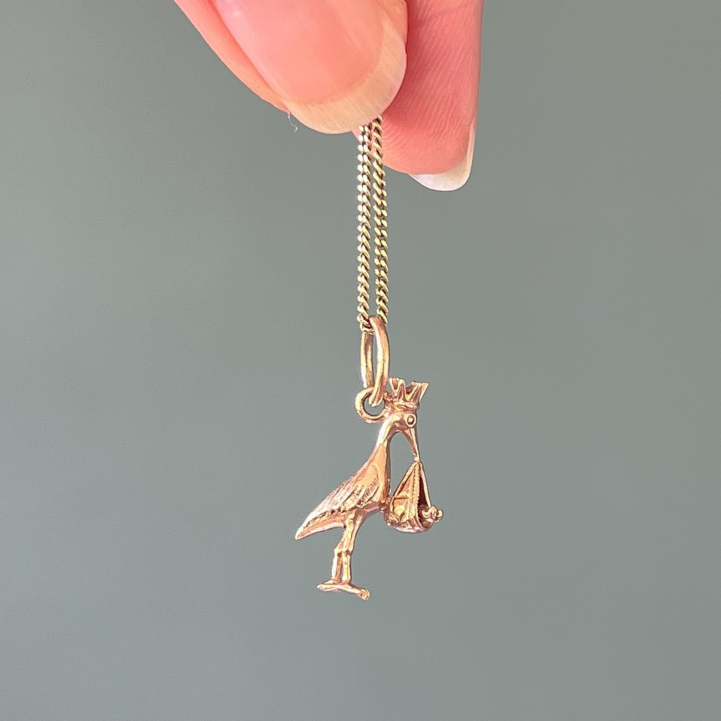 Ein Vintage-Storch aus 9 Karat Roségold mit einem Baby-Charm-Anhänger. Der Storch trägt ein Baby in einem Stoffbündel, das an seinem Schnabel baumelt. Der Charme ist mit seinen feinen Details von der Krone bis zu ihren Füßen wunderschön