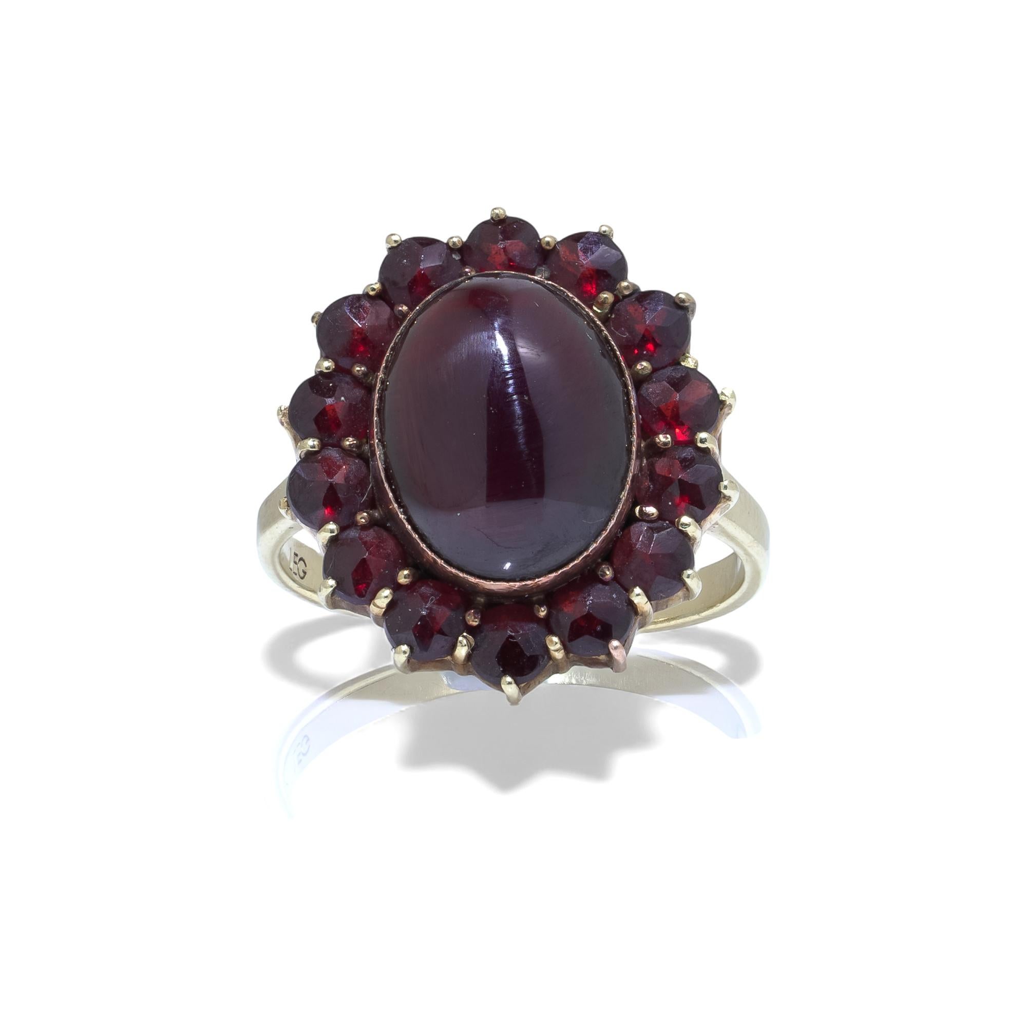 A vintage 9kt gold garnet cluster ring featuring a striking oval garnet cabochon of approximately 5 carats, surrounded by fourteen faceted garnets of approx. 0.10 ct each. The ring displays deep red, natural garnets in a classic cluster arrangement,