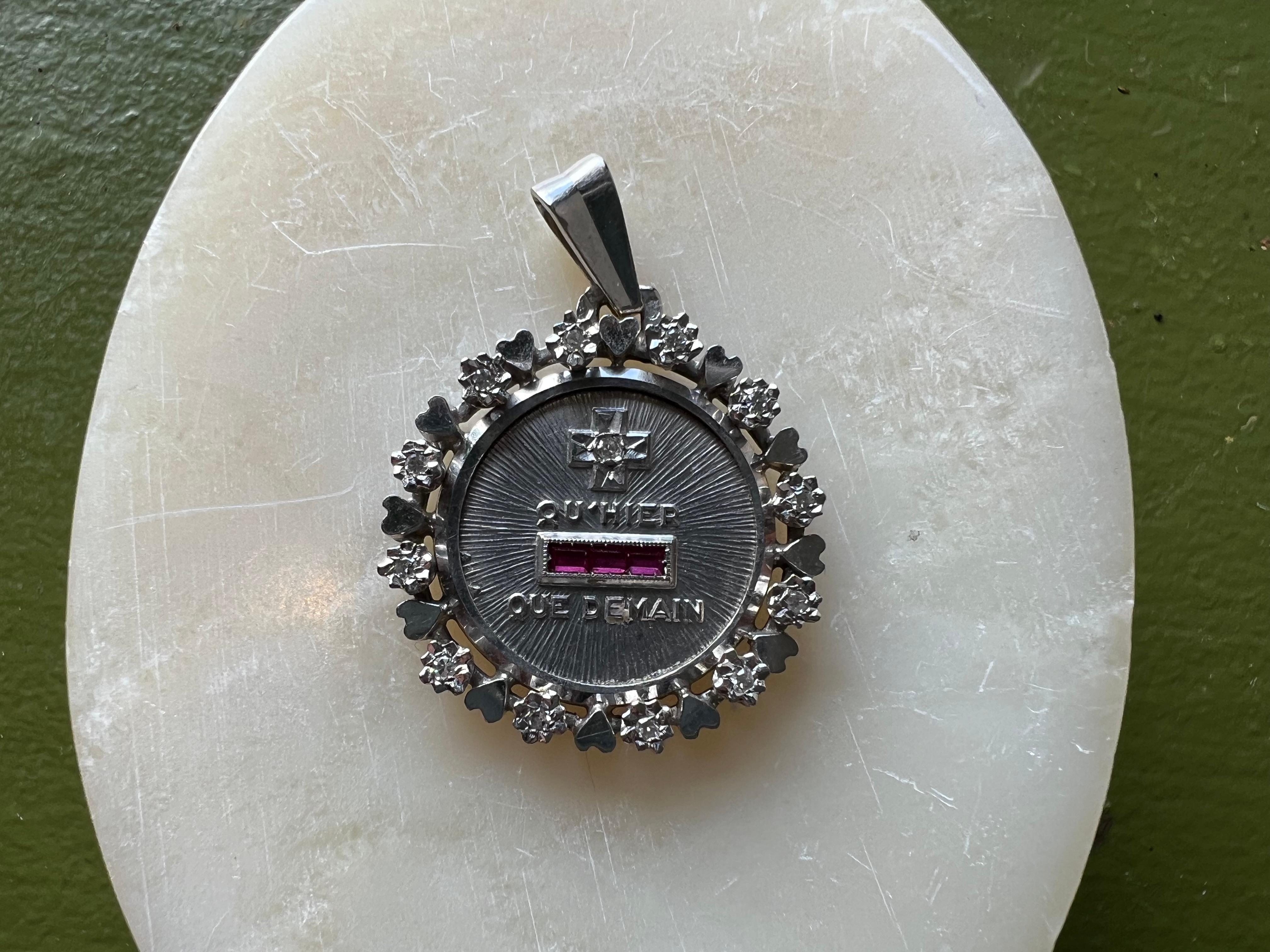 This is a very special edition of the A. Augis Love charm. 

The text reads:  “Plus qu'hier, moins que demain” AKA “More than yesterday less than tomorrow”. 

This comes from a famous poem entitled ''Les Vieux'' by Rosemonde Gérard.

(For, you see,