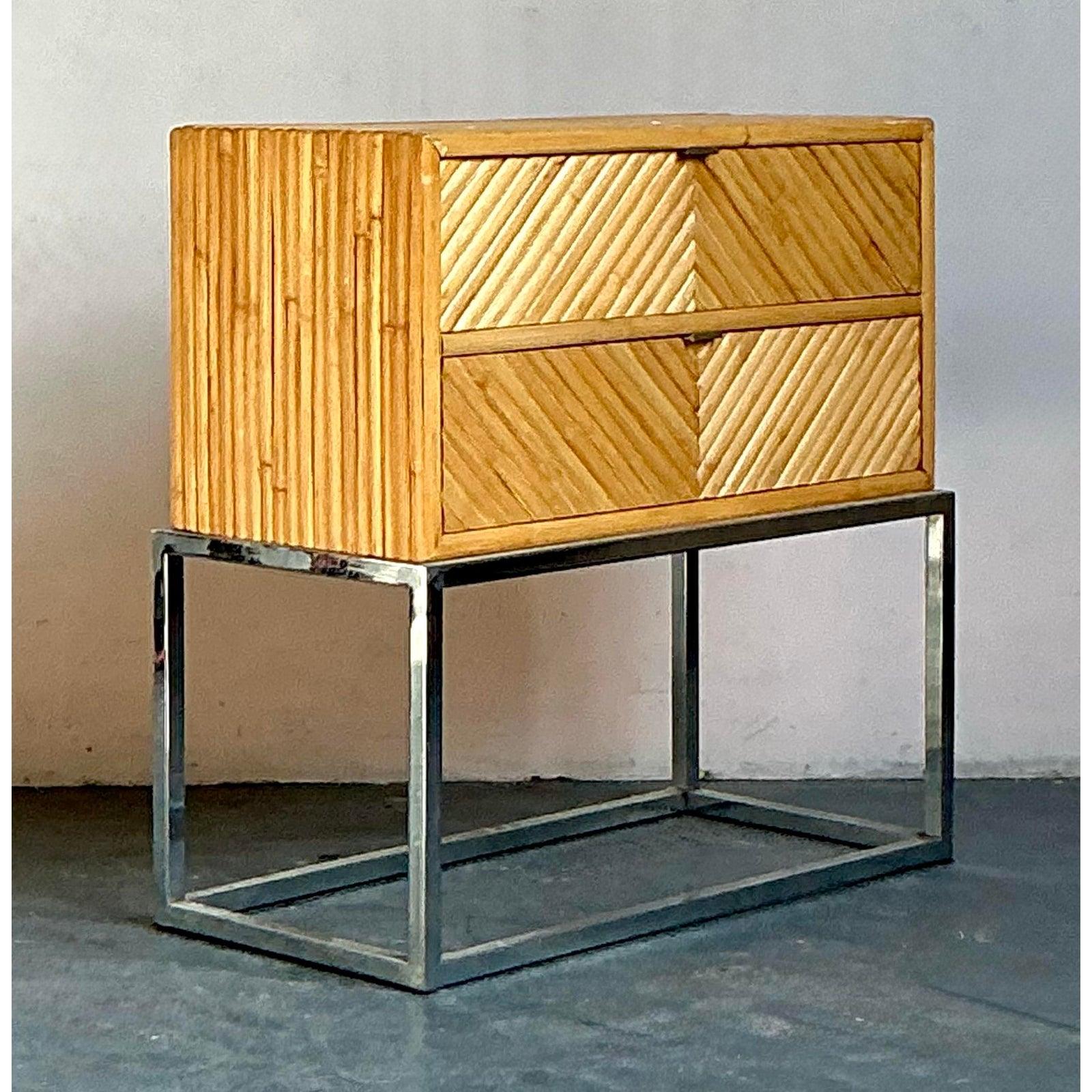 This distinctive vintage console or side table features a classic Mid-Century tropical design updated with bold geometry and industrial flair. The body is entirely clad in split bamboo or pencil reed, intricately arranged in a sophisticated chevron