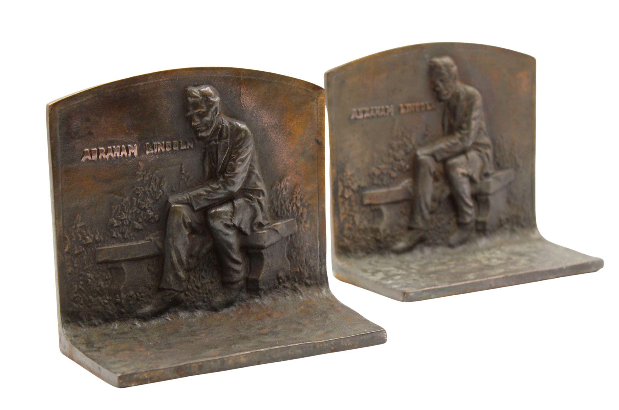 Präsentiert wird ein Paar von Vintage-Buchstützen, die Abraham Lincoln auf einer Bank sitzend darstellen. Die Szene ist als Relief auf der Vorderseite der Buchstützen abgebildet, mit dem Text 