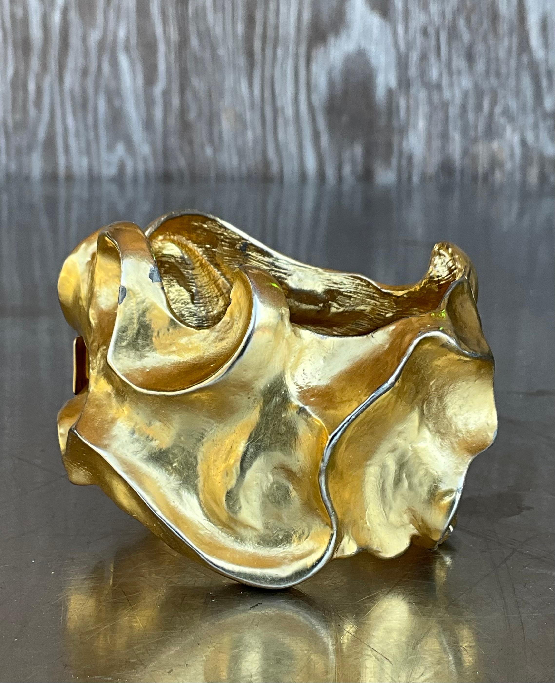 Questo bracciale astratto vintage in tonalità oro è un pezzo di grande effetto che incarna un design audace e un'eleganza senza tempo. Realizzato con una silhouette scultorea e libera, il bracciale presenta un motivo astratto di linee fluide e