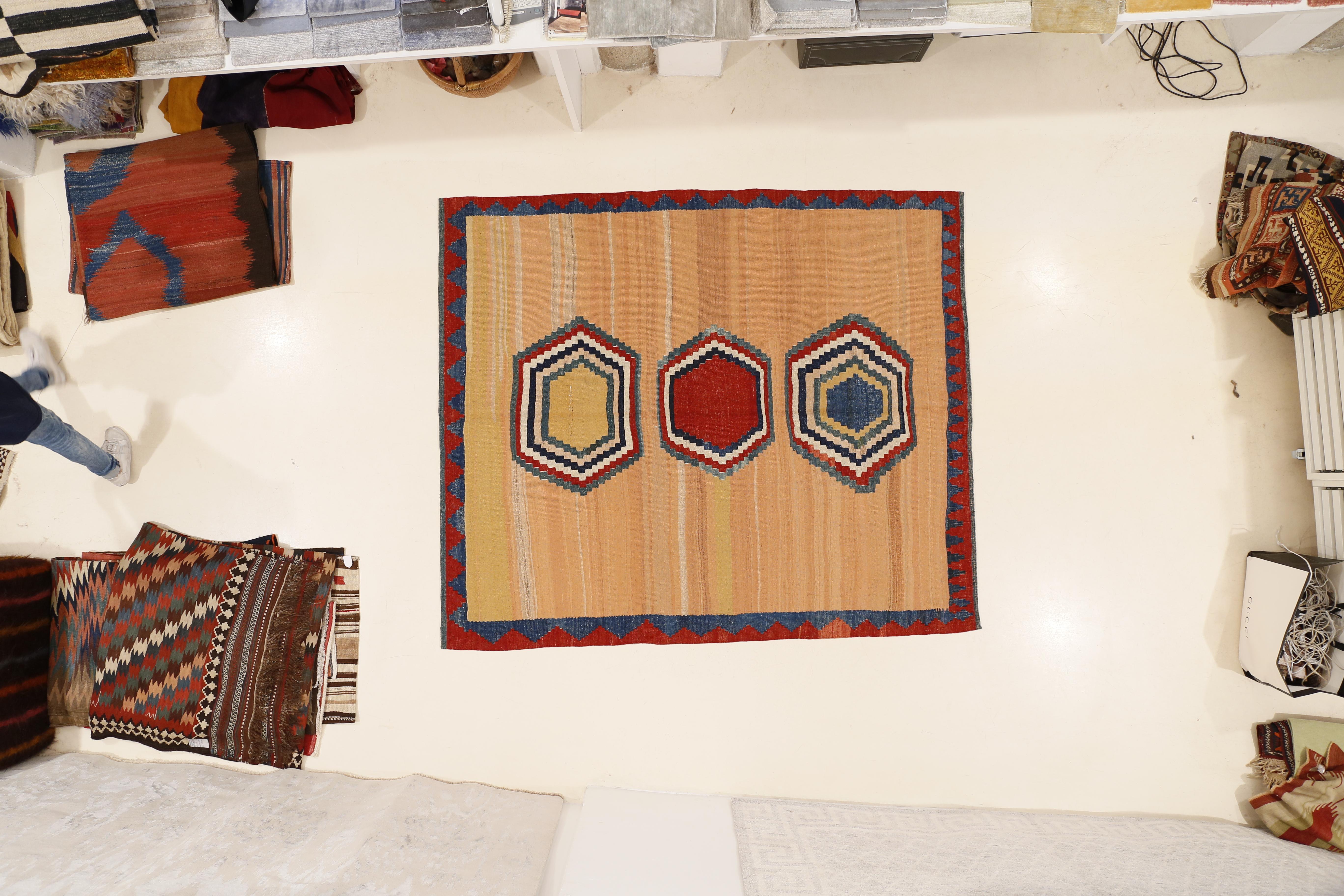 Un kilim tribale grafico caratterizzato da una semplificazione del motivo, ridotto a tre esagoni concentrici policromi disposti su uno sfondo albicocca striato. Caratterizzato da una texture robusta, paragonabile a quella di un tappeto a pelo