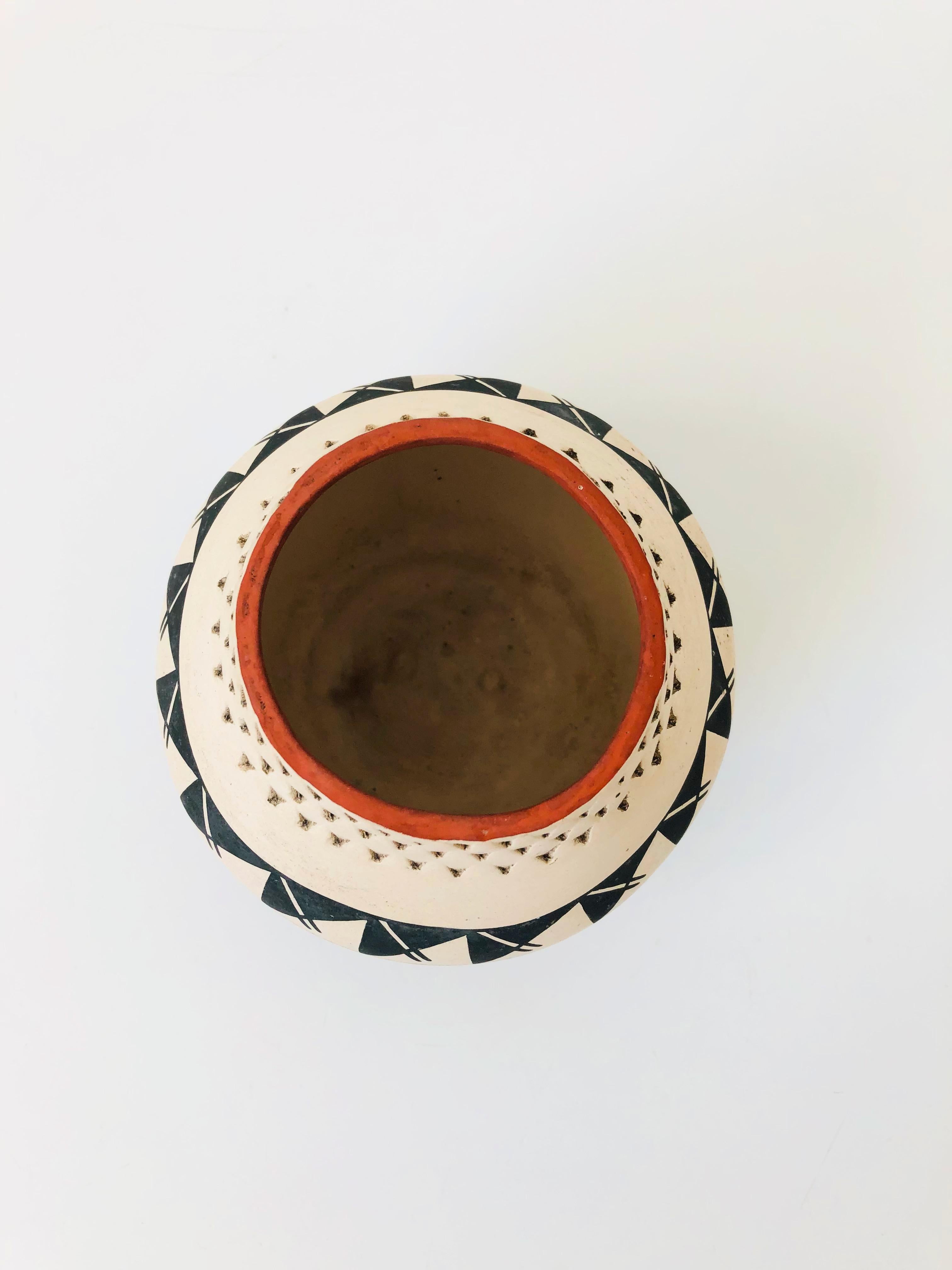 A vintage hand made Acoma pueblo pottery vase with a graphic hand painted design in black and terra cotta on an off-white background. A perforated texture to the neck of the vase adds interest. Signed on the base by R Juanico.
 