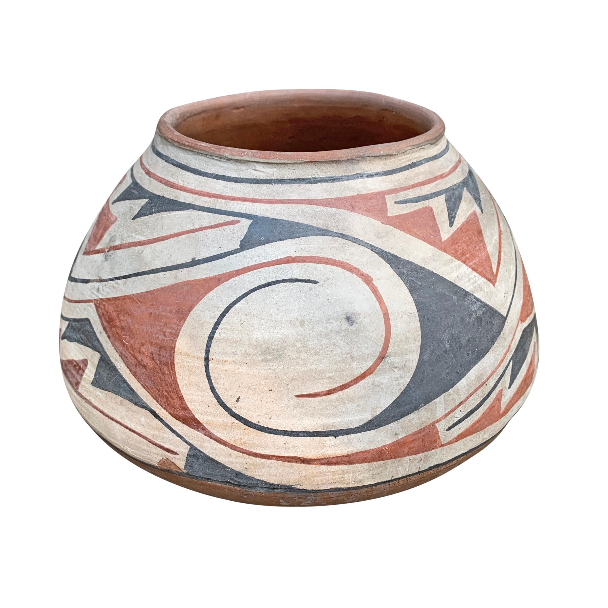 A striking vintage Casa Grandes pottery vase with a shallow bottom and a wide belly, and decorated with a red and black swirling wind pattern repeated three times around the pot. This pot dates to the 1940s when Prehistoric designs became popular.