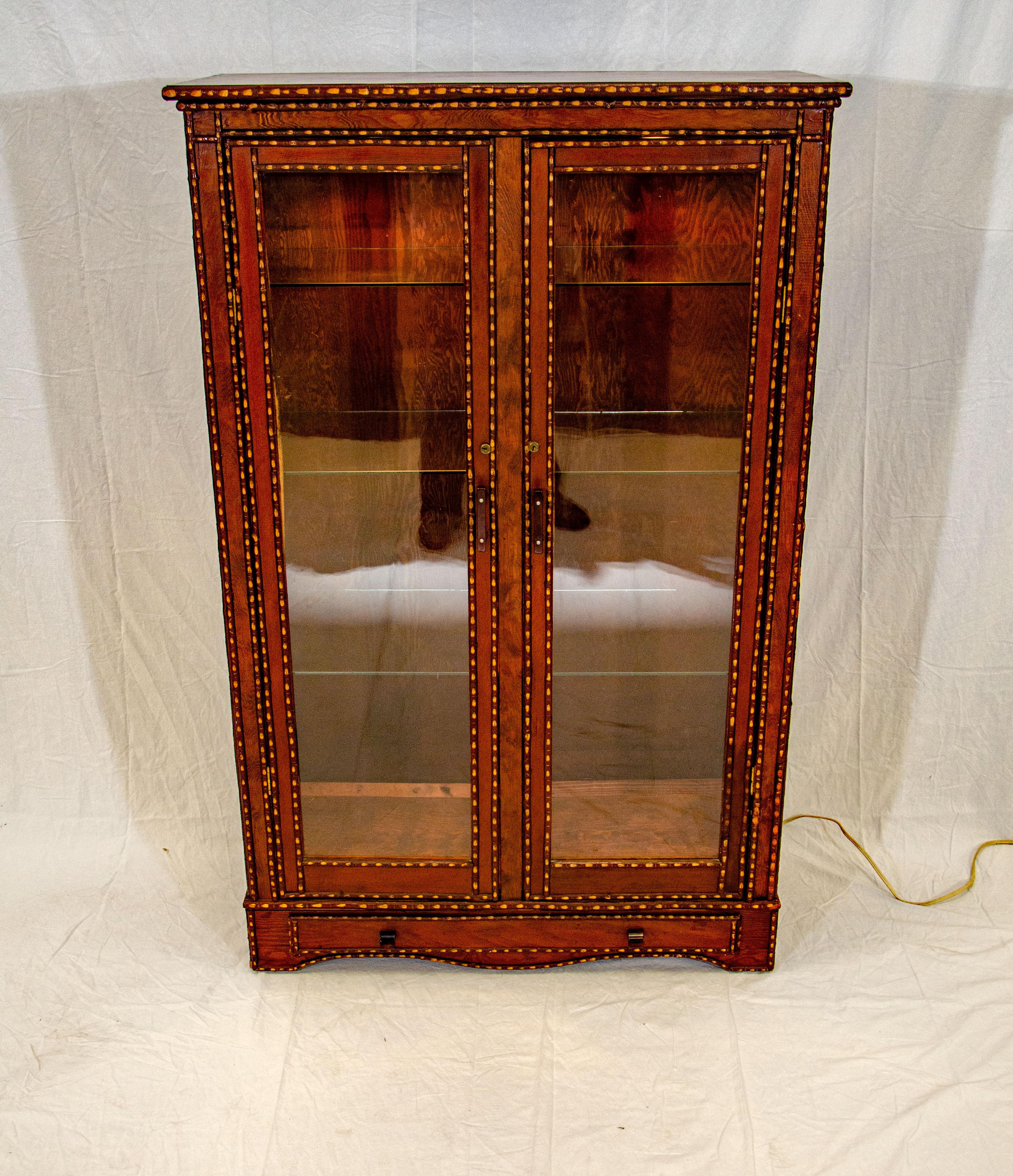 This unusual cabinet in the country cabin style can be used as a bookcase or dish display. The shelves are glass and there are lights installed. The handles on the doors and bottom drawer are a dark apple juice bakelite color. The interior spaces