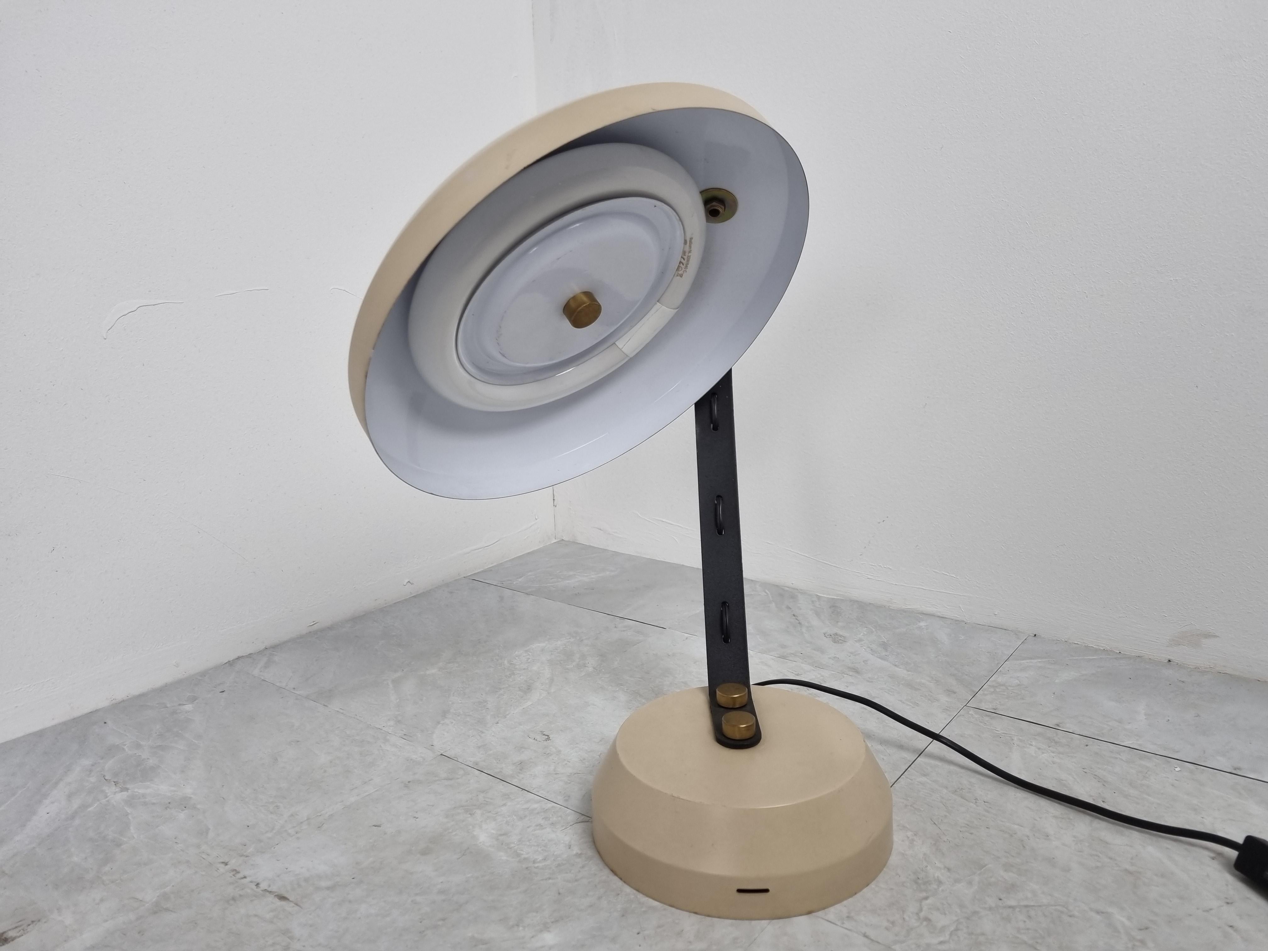 Vintage adjustable desk lamp with a neon light bulb.

Beige and black metal base and lamp shade with brass details.

Nice quality desk lamp from the seventies which is very adjustable, so the ideal desk lamp. It also emits plenty of