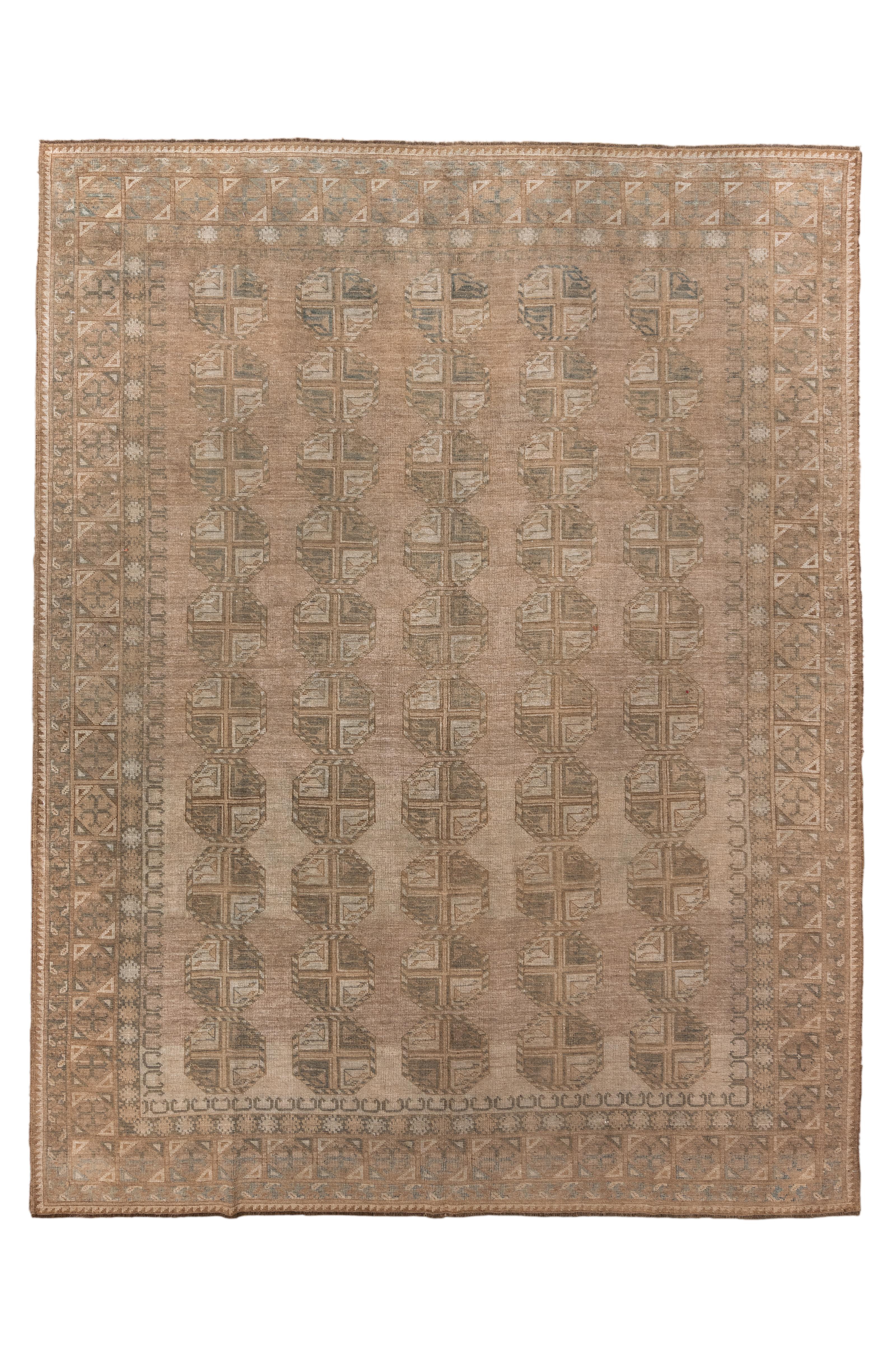 Un étonnant tapis afghan vintage présentant un motif de gul allover - classique dans le tissage afghan - disposé en colonnes ordonnées sur un fond taupe chaud. Cette pièce rayonne de douceur grâce à sa palette sourde de sable, de beige, de gris doux