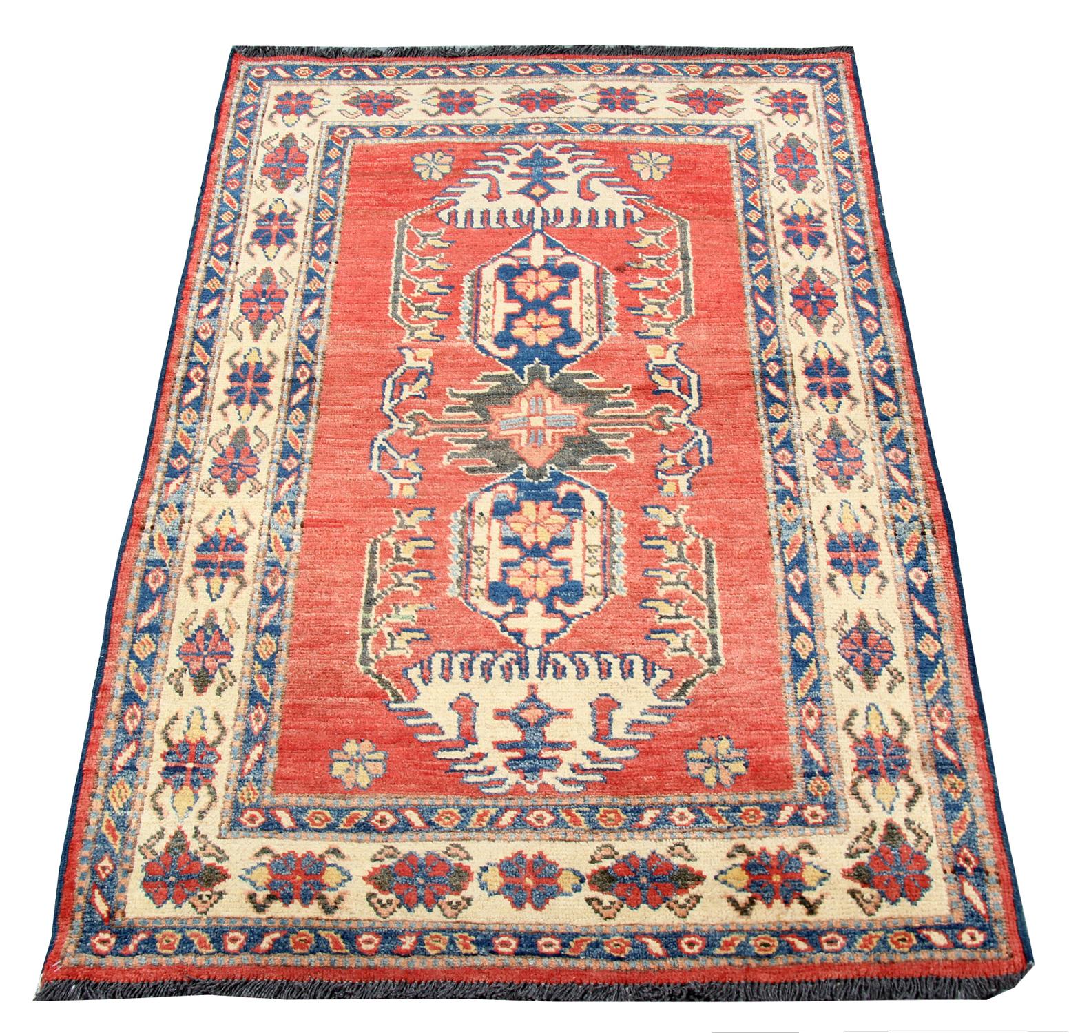 This fine wool rug was woven by hand in Afghanistan in the early 2000s. The central design features a traditional geometric motif design woven in accents of cream blue and green on a rich red background. Both the colour and style in this piece are