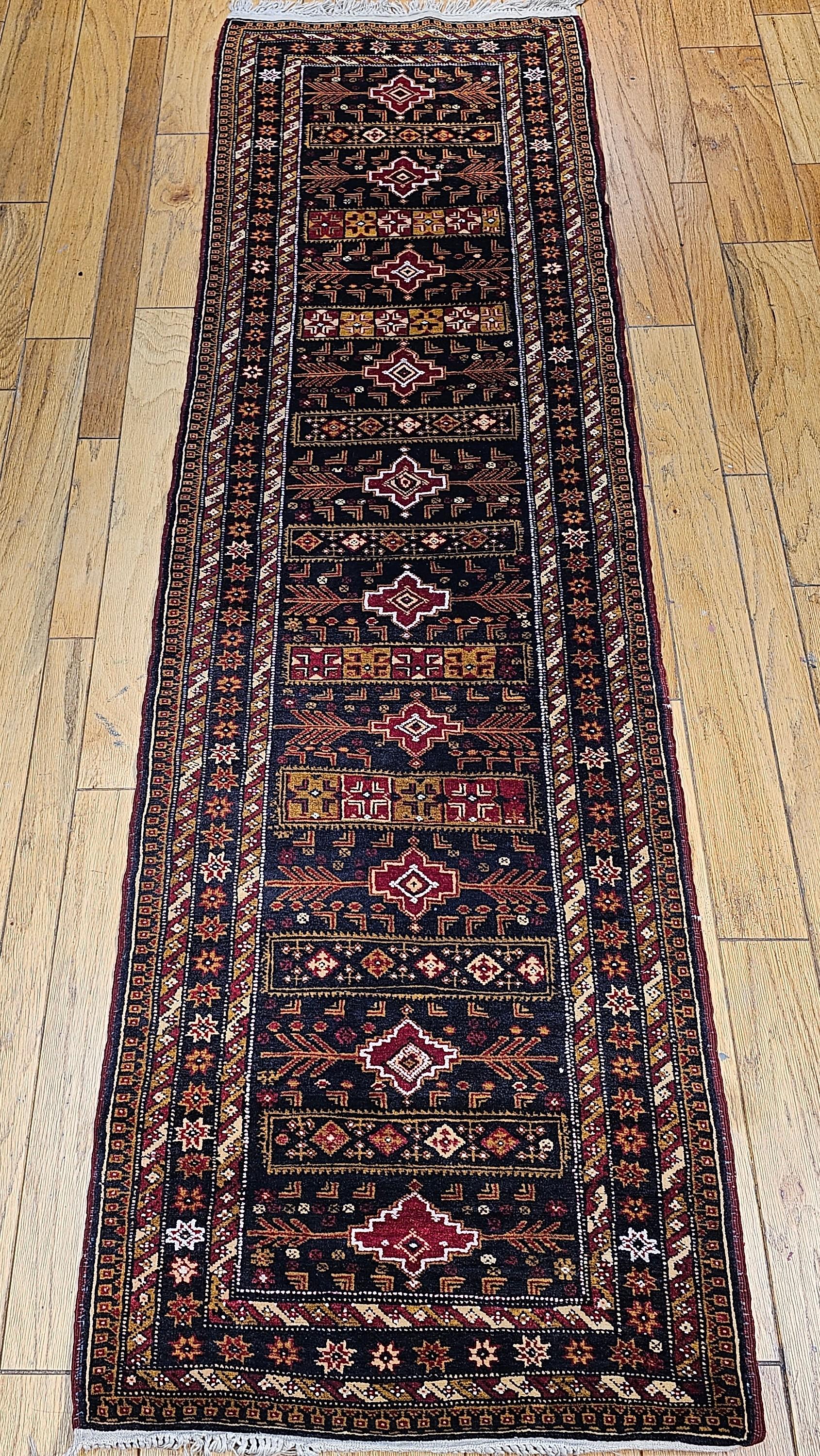 Vintage Afghan Tribal Runner in geometric pattern circa the mid 1900s.  The field in this Afghan tribal runner is a dark midnight blue color with designs in gold, red and brown colors throughout the field and the borders.  The surprising element is