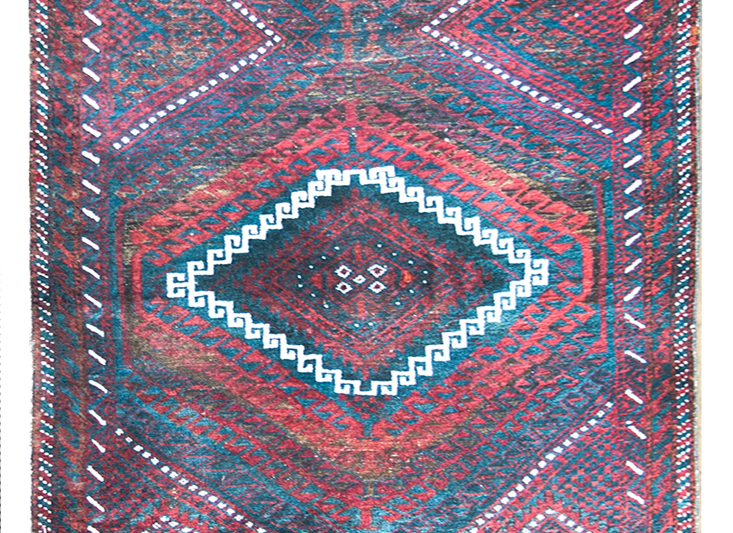 A wonderful mid-20th century Afghani Baluch rug with three large diamond medallions with stylized scrolling vine patterns woven in white, black, crimson, and orange, and surrounded by a complex border with even more stylized floral shapes.  