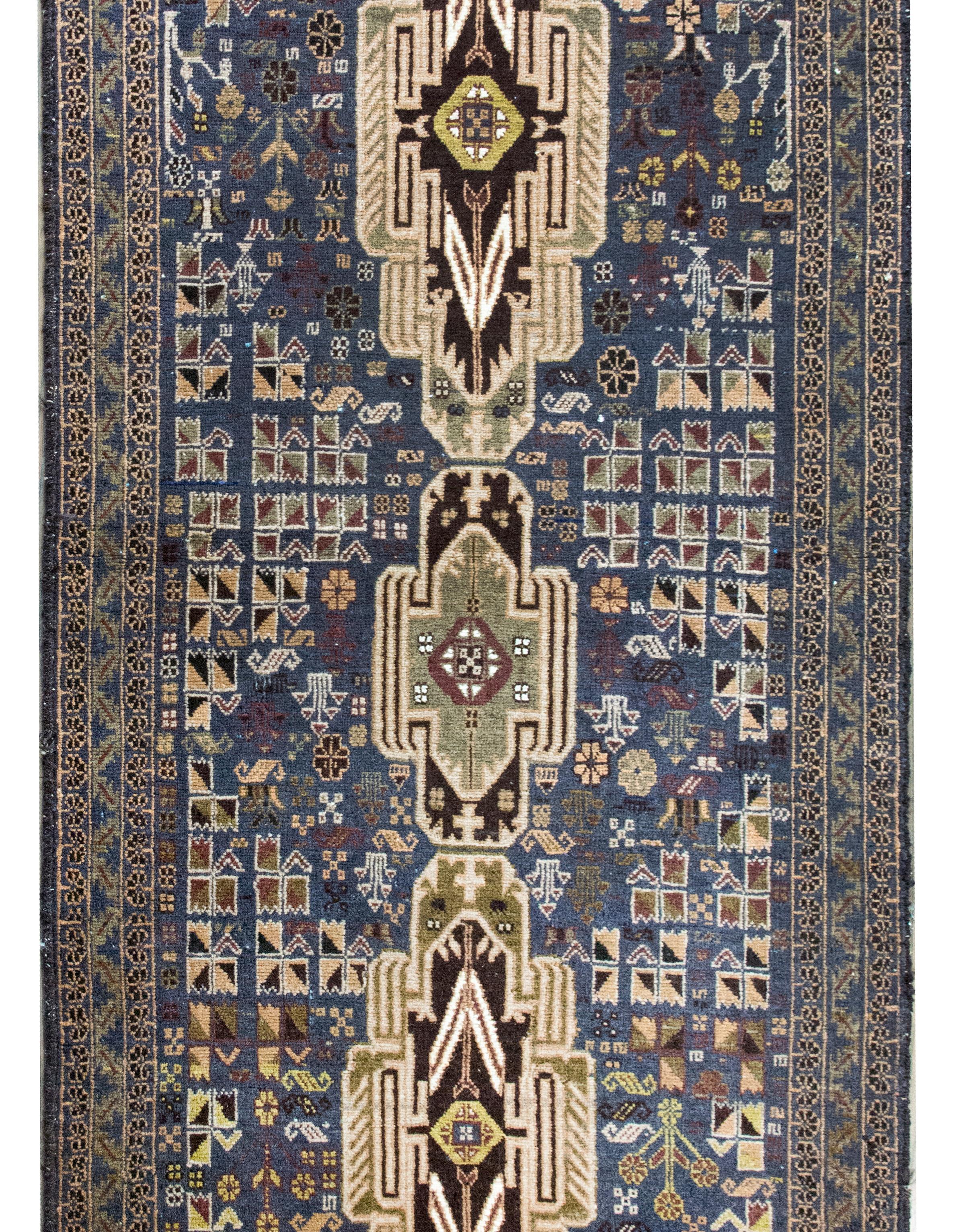 A wonderful late 20th century Afghani Baluch Rug with three large geometric, Art Deco inspired, medallions living amidst a field of stylized flowers, surrounded by a simple border with more stylized flowers and leaves, and all woven in beautiful