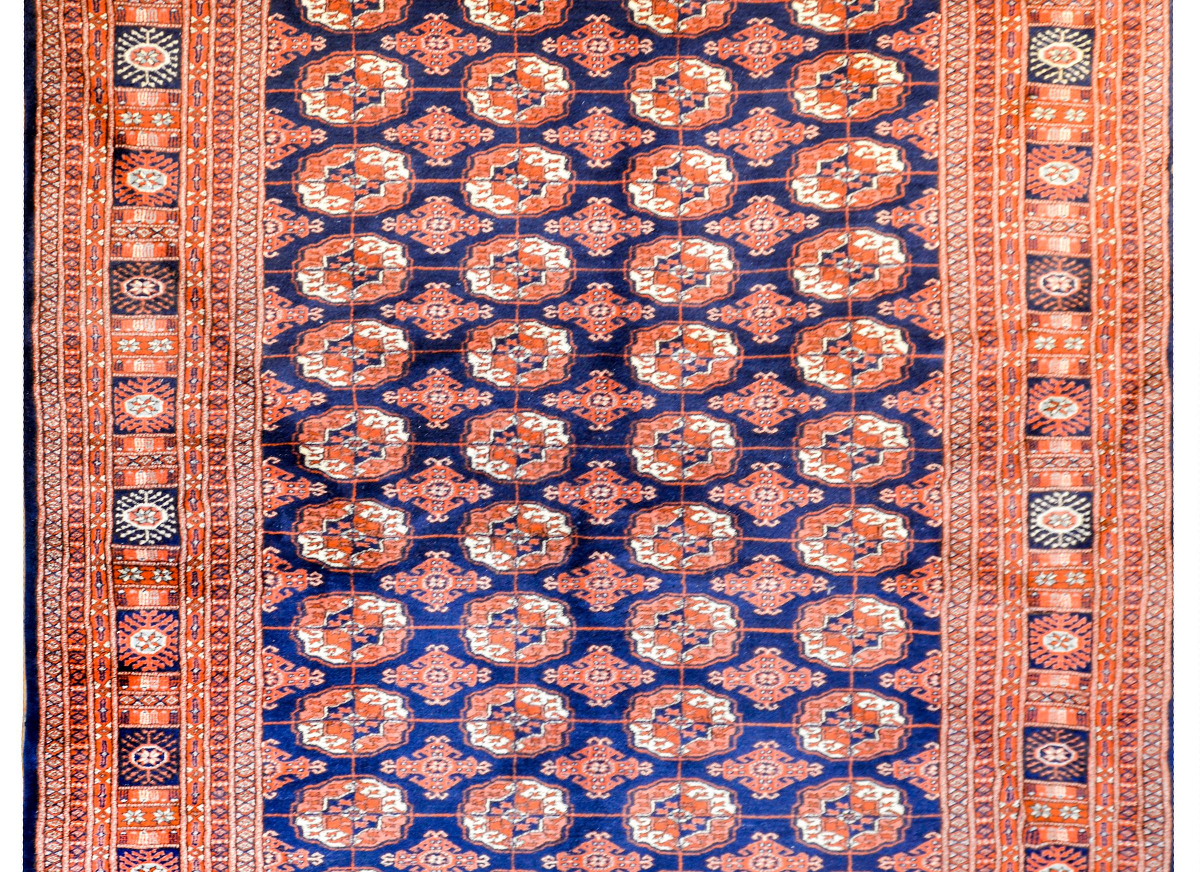An exceptional vintage Afghani Bokhara rug with an all-over stylized floral medallion pattern woven in white, indigo, and orange vegetable dyed wool, on a dark indigo ground. The border is extra wide, comprised of multiple petite and wide stylized