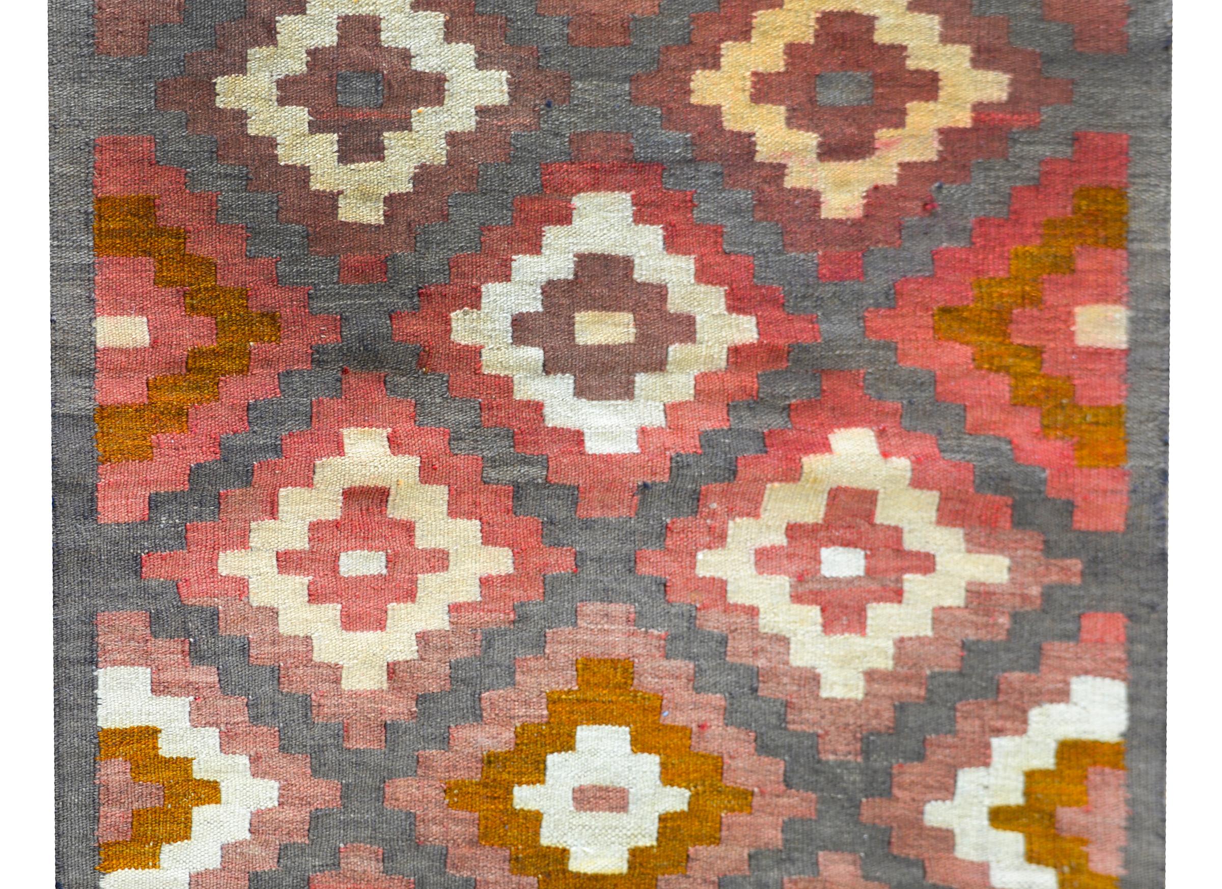 A wonderful vintage Afghani Kilim rug with an all-over diamond pattern woven in myriad colors including crimson, gold, gray, and white, and with ends woven in simple striped patterns.