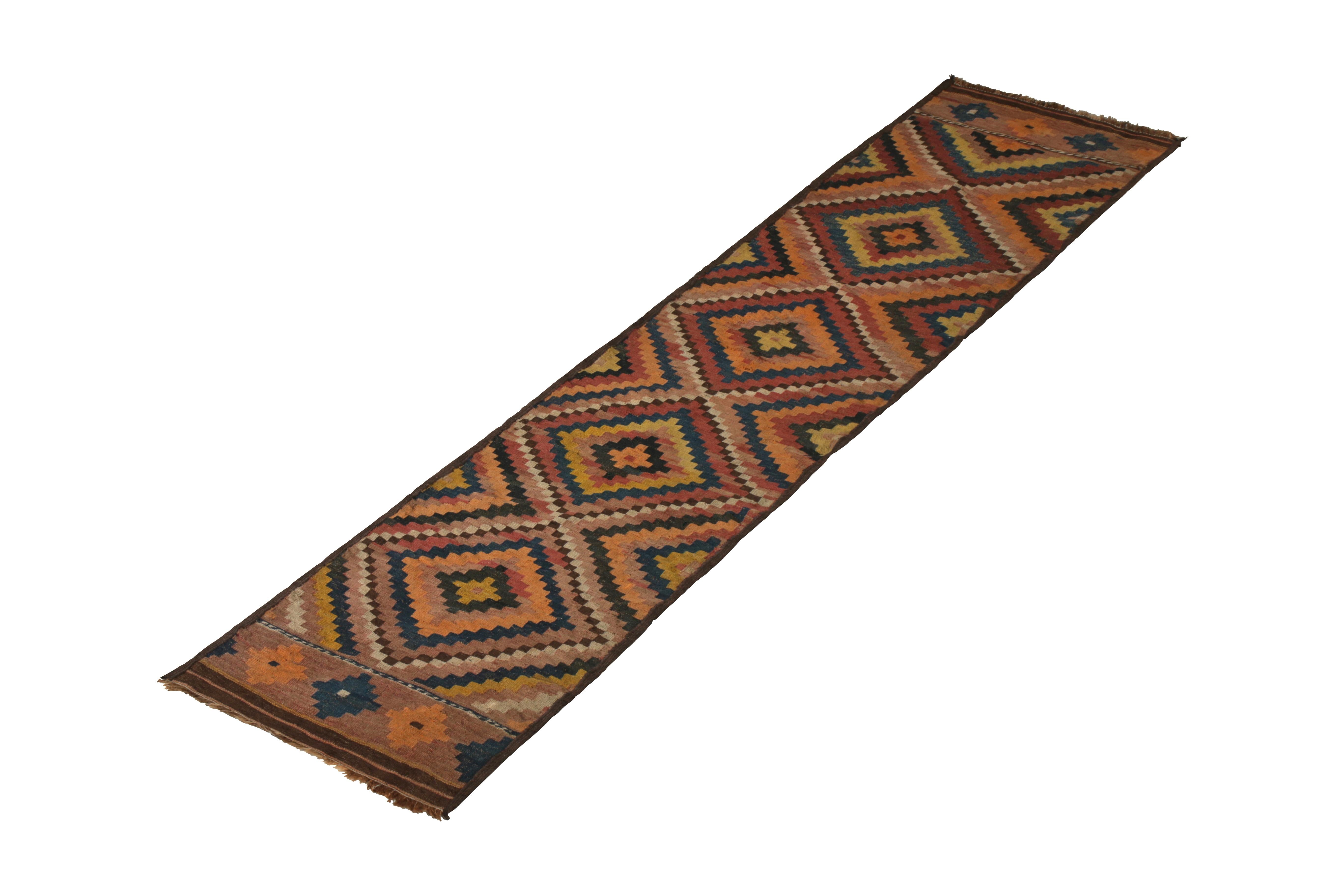 Flat-woven in wool originating circa 1950-1960, this vintage Kilim runner connotes a midcentury Afghan rug design borrowing heavily from celebrated tribal themes, including a bold diamond pattern in complementary orange, red, yellow, beige brown and