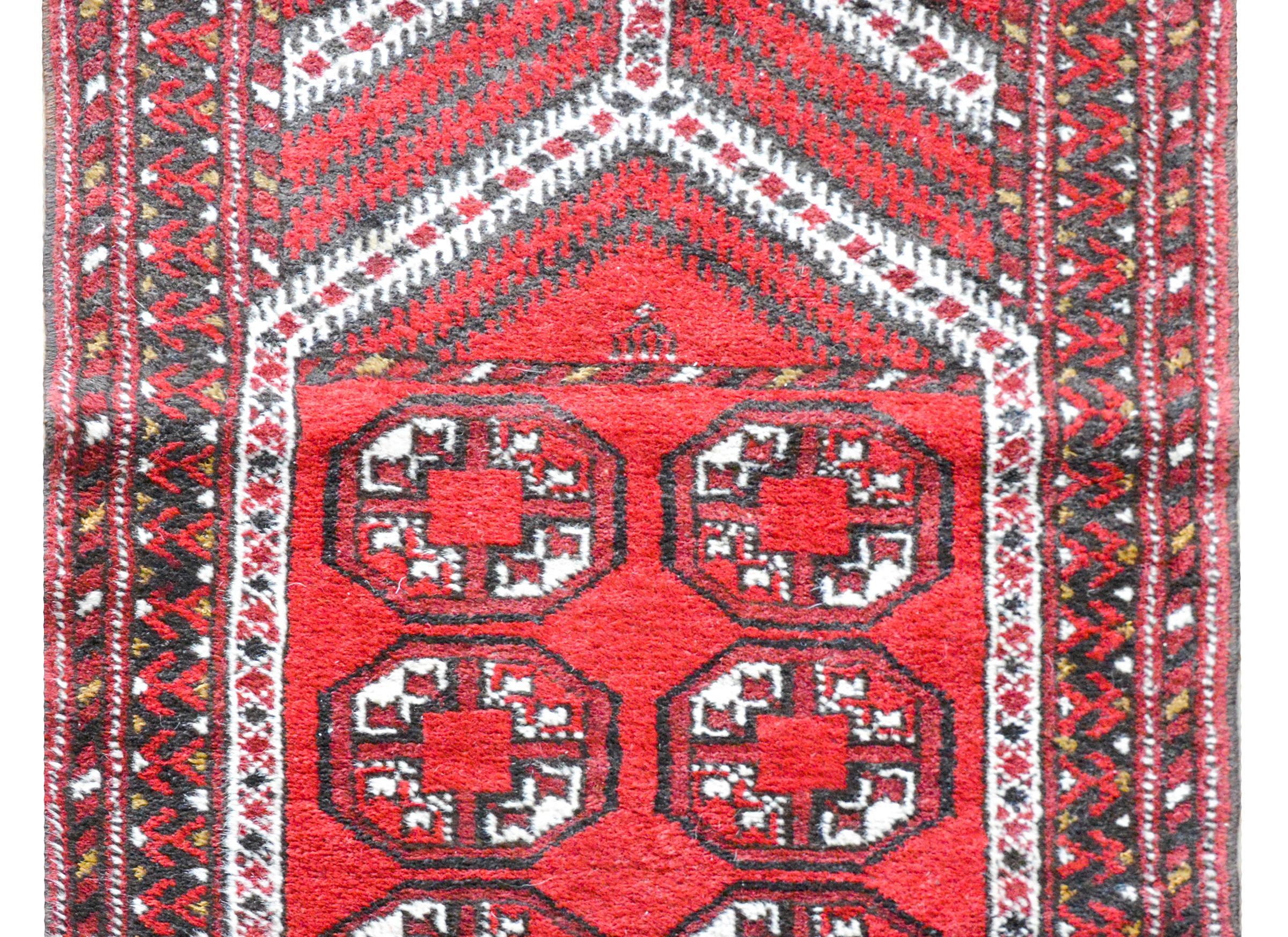 A charming vintage Afghani Turkmen prayer rug with a geometric pattern woven in crimson, black, and white, and surrounded by a border composed with three thin geometric pattered stripes.
