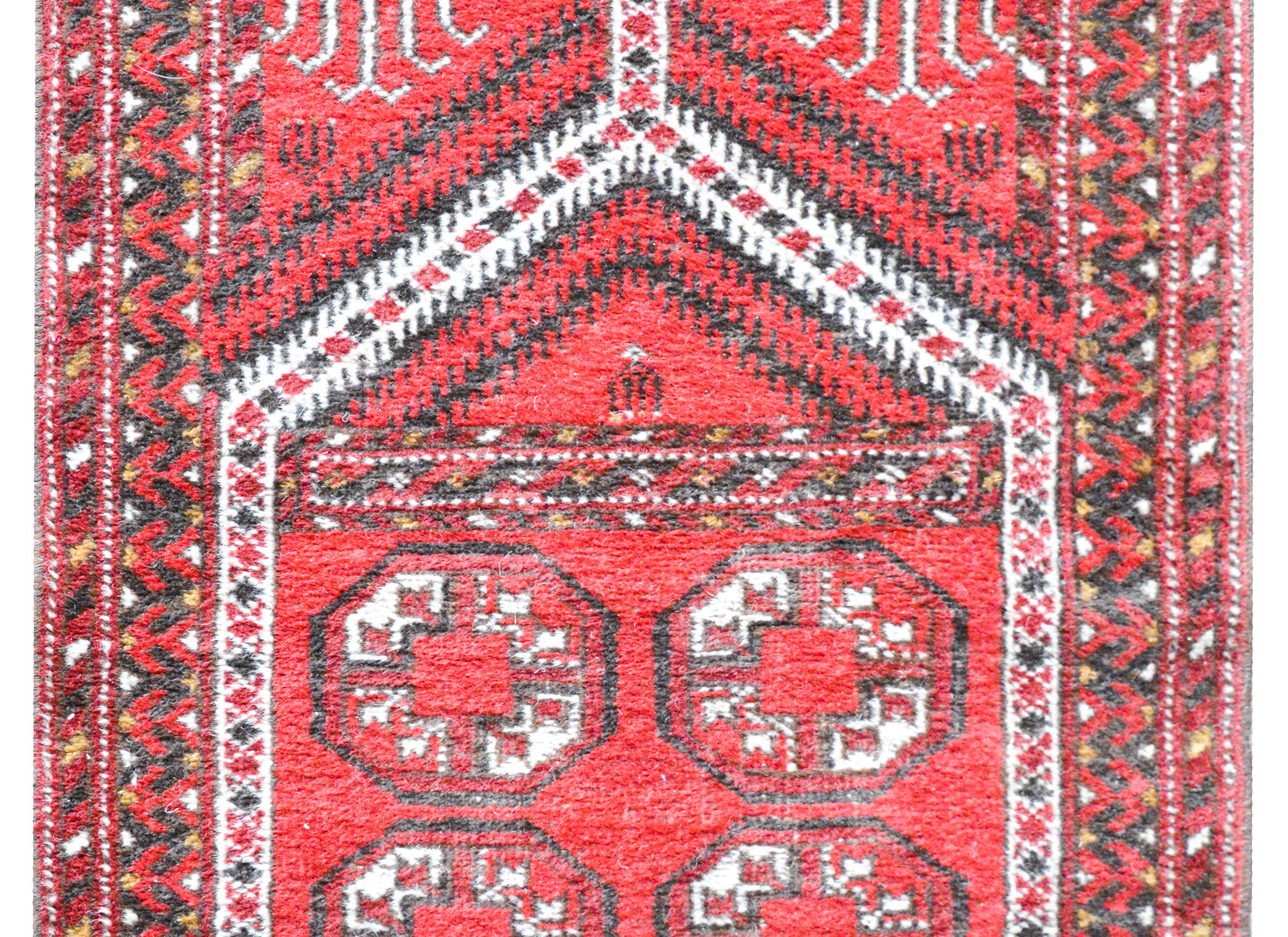 A wonderful vintage Afghani prayer rug with several geometric patterned stripes and medallions all woven in crimson, black, white, and gold, and surrounded by a border composed of multiple petite floral partnered stripes.