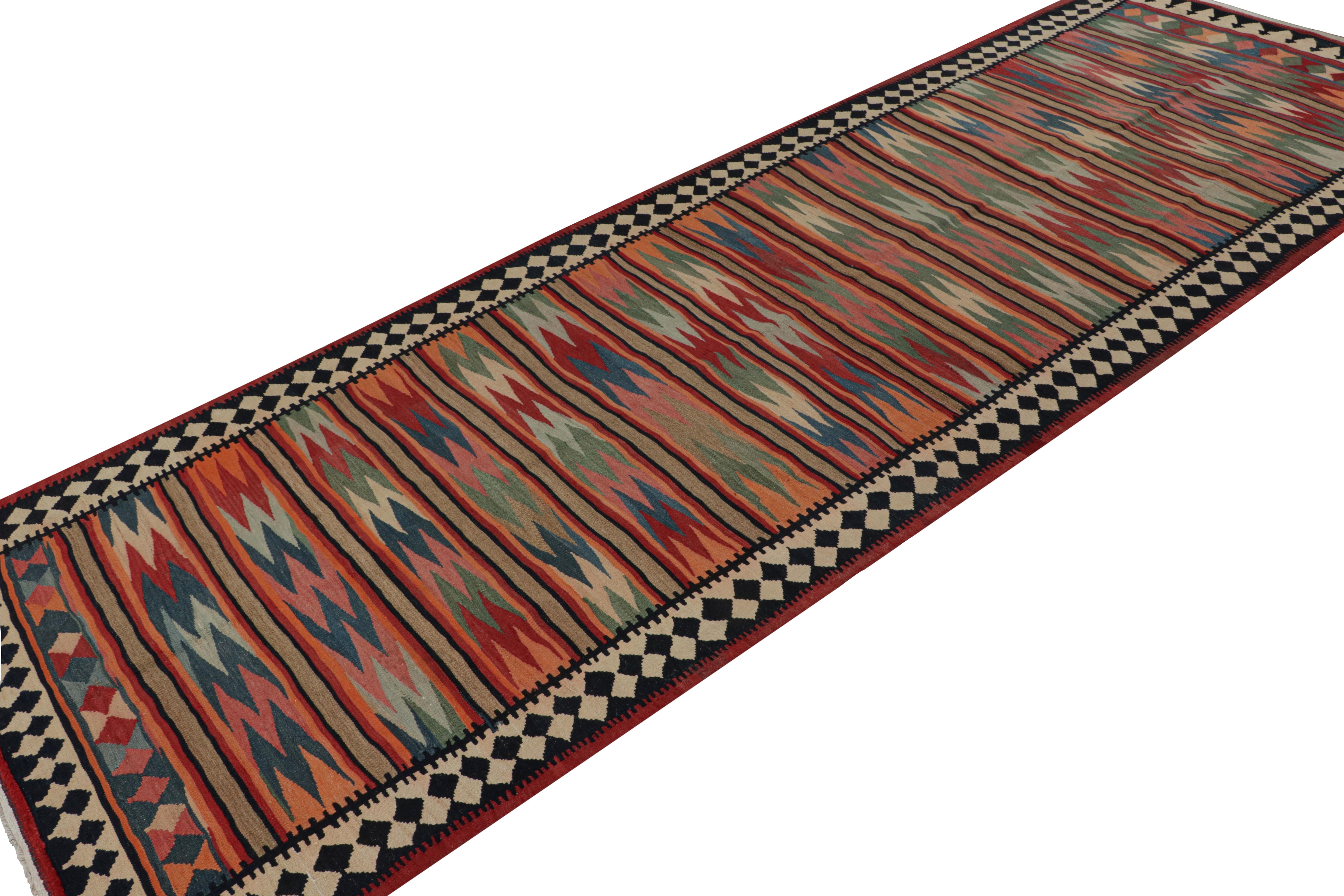 Handwoven in wool, circa 1950-1960, this 5x14 vintage Afghani tribal kilim rug, is nearly a gallery runner-sized artwork. With serrated geometric patterns, its design features a vibrant color palette of red, beige/brown, green, and blue. 

On the