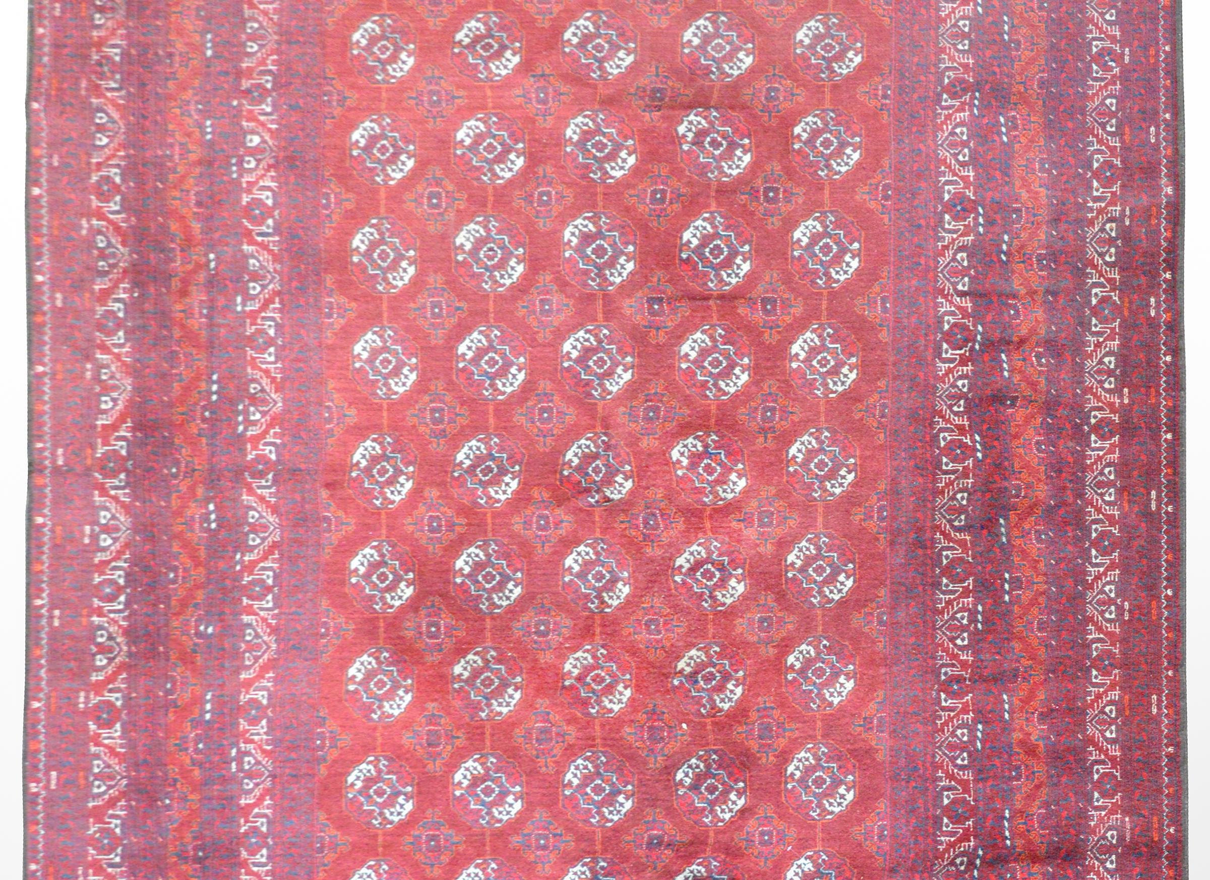 A beautiful 20th century Afghani Turkoman rug with a repeated circular pattern woven in crimson, orange, white and indigo surrounded by a wide border containing multiple geometric and floral patterned stripes.