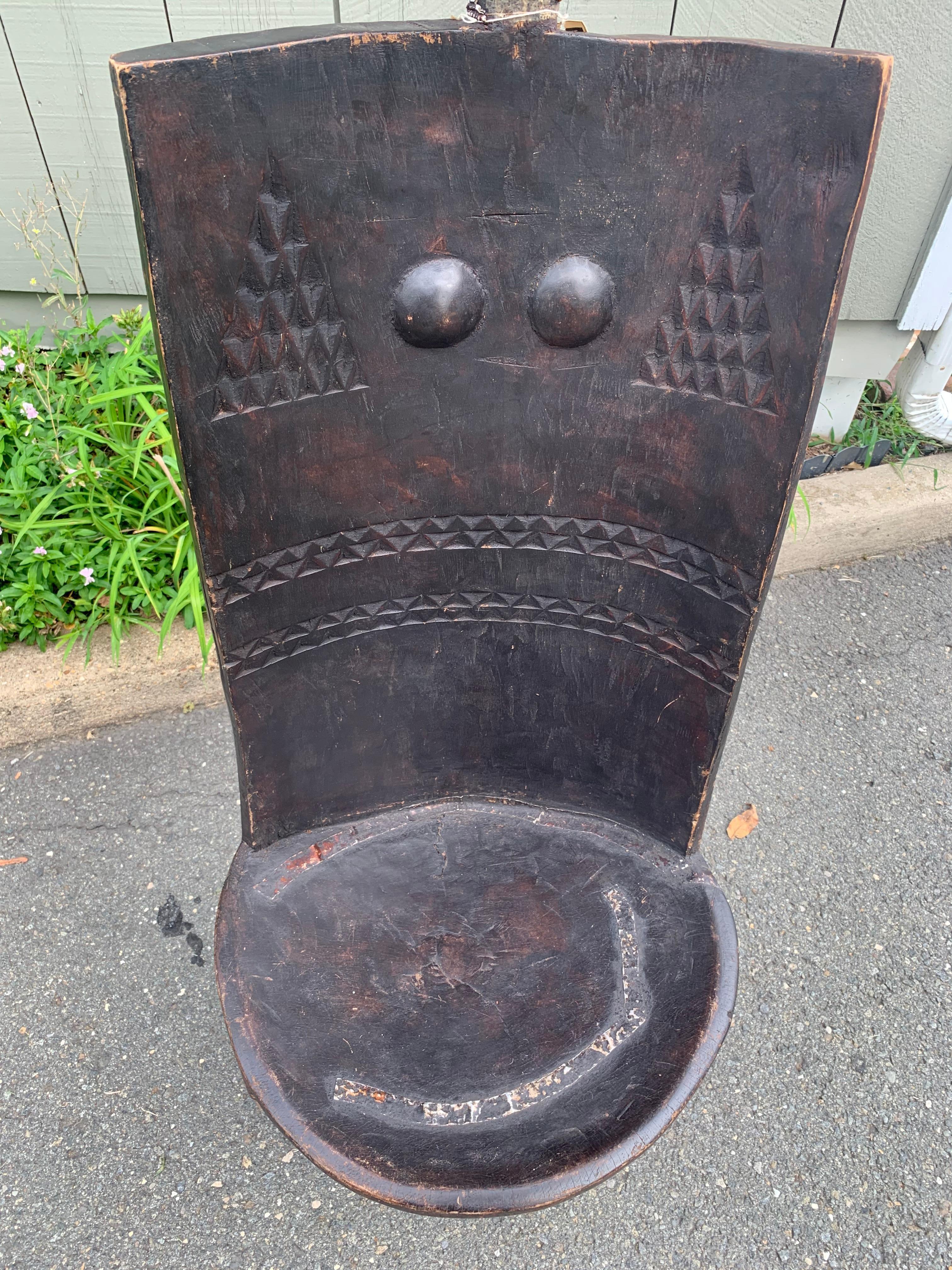 A striking African ceremonial or chief’s throne chair carved in one piece from a single tree trunk having artful head at the top, female breasts, beautiful decorative carvings and some inlaid metal on the seat. Surprisingly comfortable. The chair is