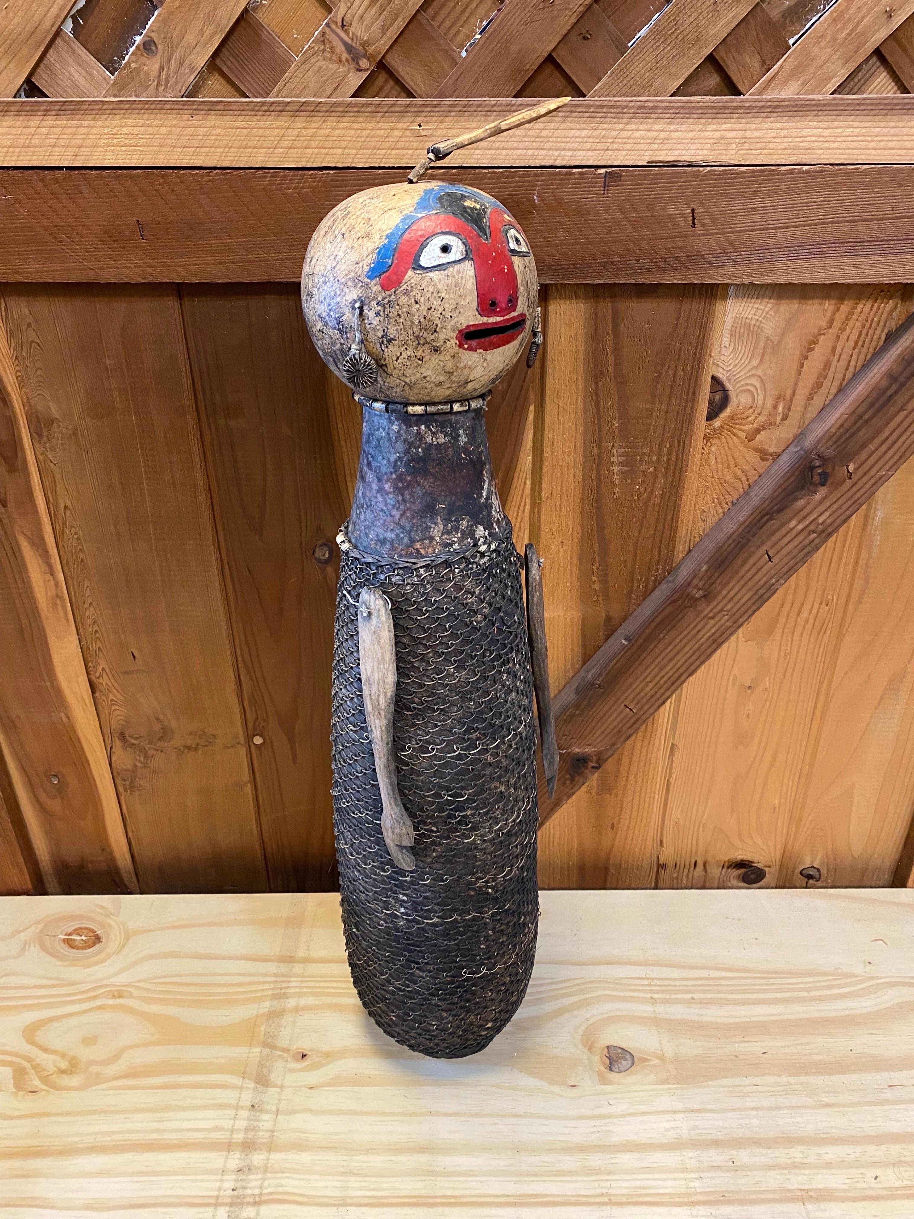 Beautiful vintage African Namji doll made from dried gourd and decorated with a rattan skirt and earrings. This precious African statue or sculpture is finished off with a red, blue and white face paint. On the top there's what looks like a hook and