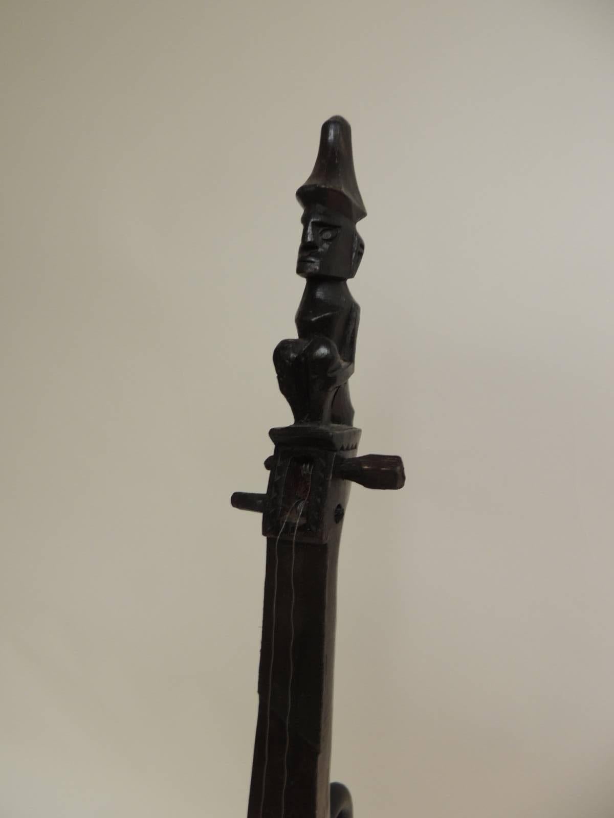 Vintage Indonesian harp instrument on iron stand, told hand-carved wood harp with carved human figure
 on top and carved face figure on the under-side of the harp. The harp is hollow inside. Dark wood stained patina.
Note: The iron stands are