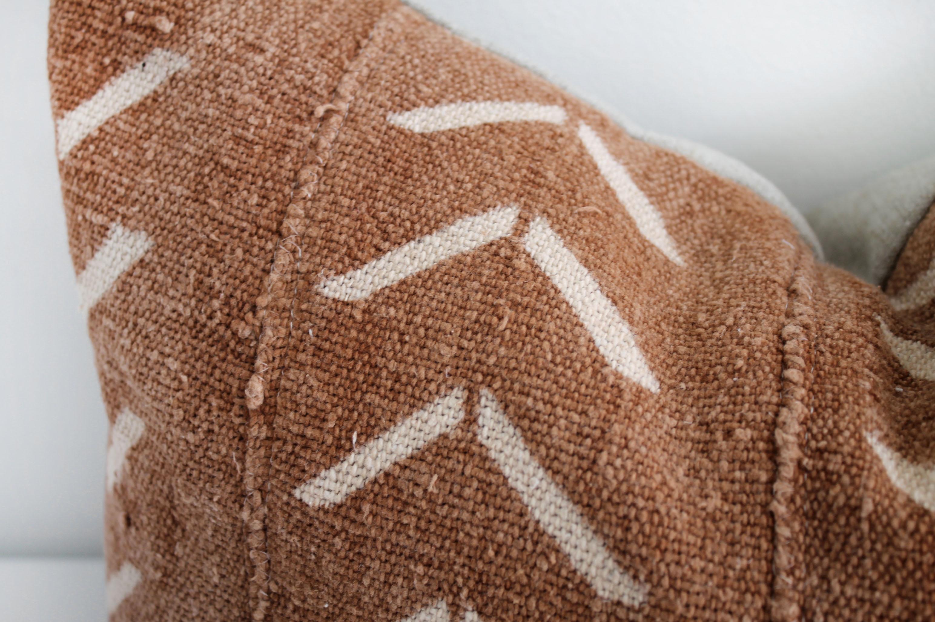 Vintage African Mudcloth pillow from Mali, Africa. A deep burnt orange rust color, with off-white arrow pattern, and features original fringe details from the original material. Sewn with a zipper closure, and natural linen backing. The inside has