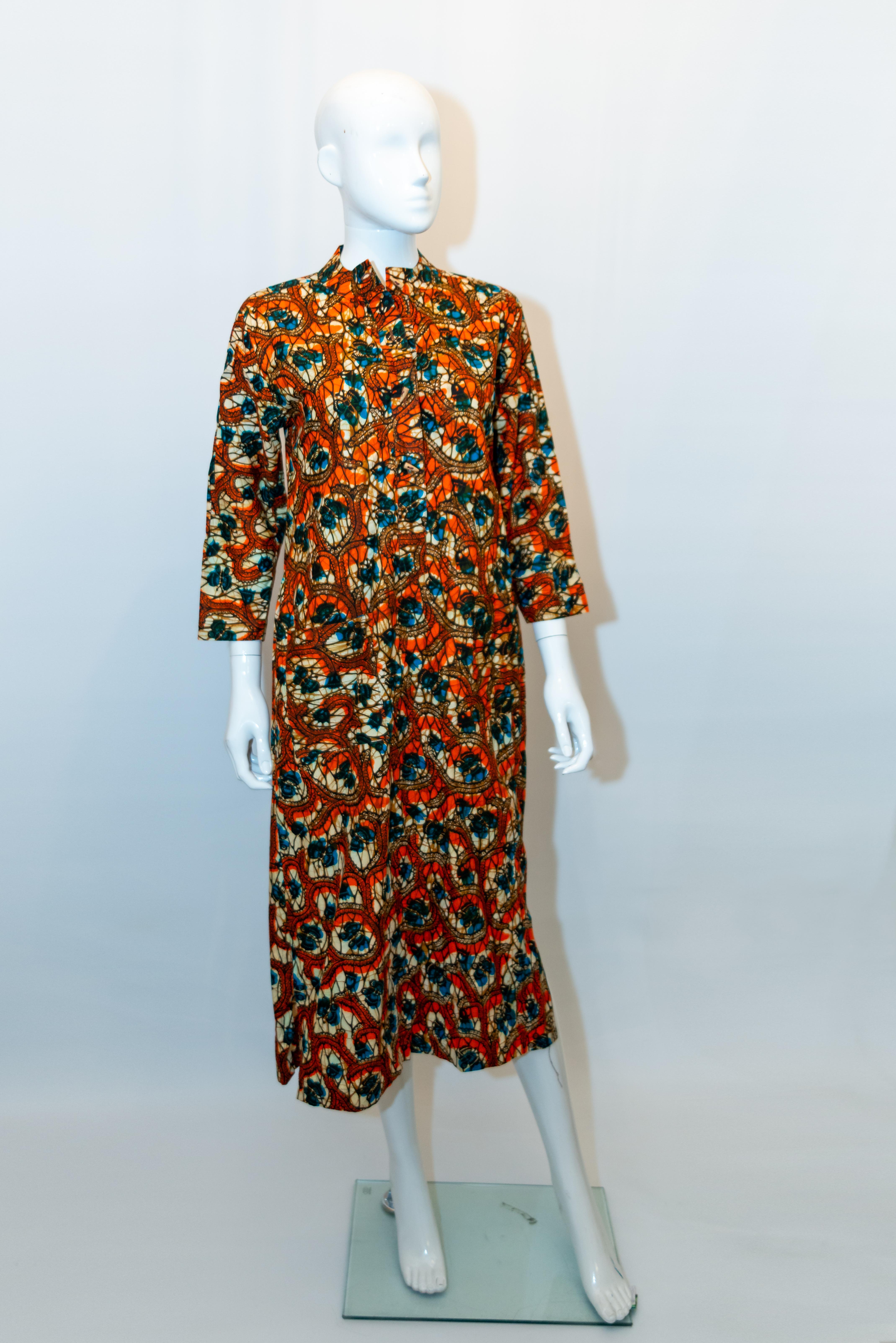 A wonderful vintage cotton dress by  Lumiere Couture of the Ivory Coast , Africa. 
The dress is in a butterfly print of blue, orange and brown and has two pockets on the front, a button front opening ,elbow length sleaves and a 9'' slit on either