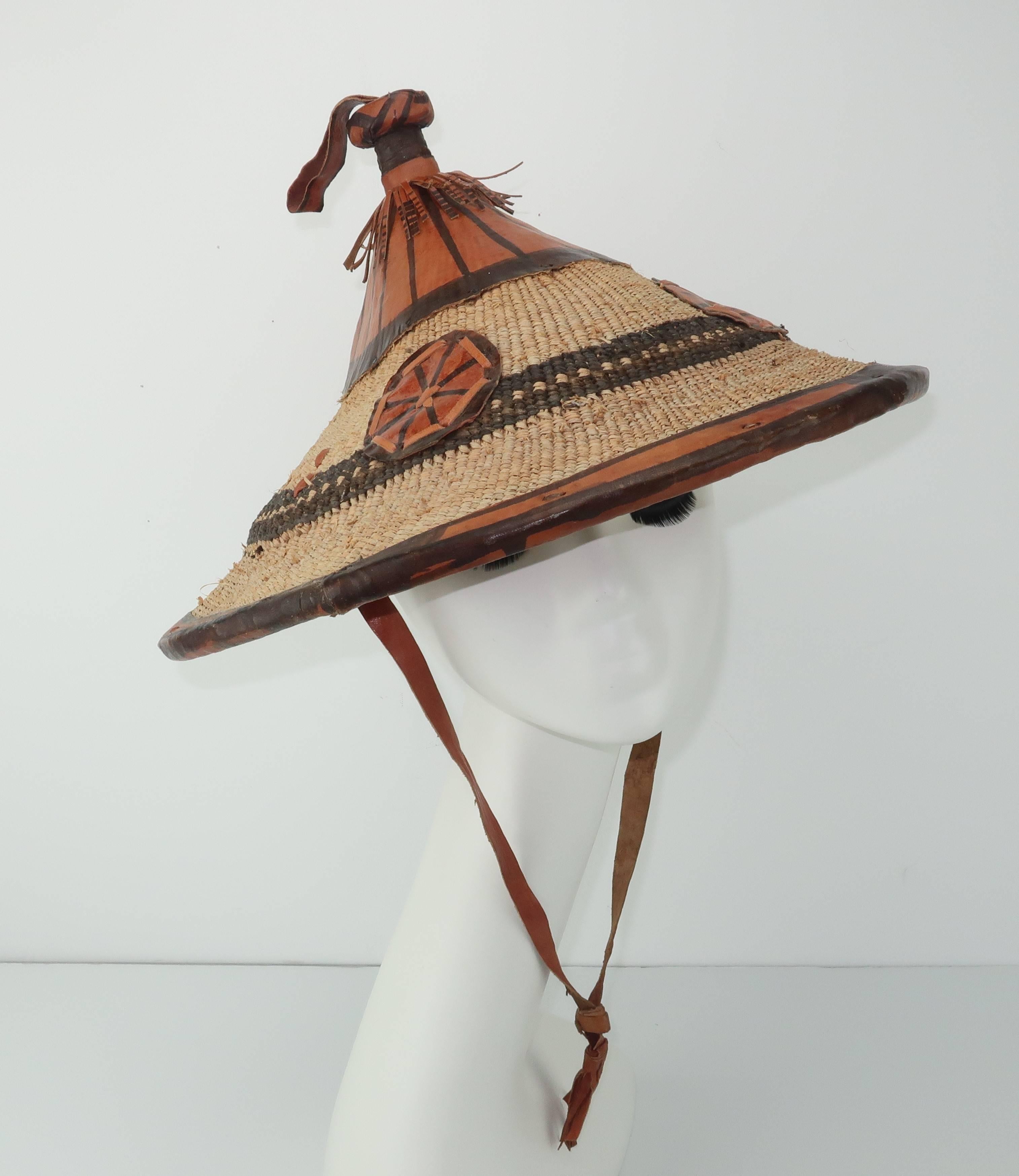Get the look of a world traveler with this vintage African hat hand made from a tight straw weave with painted leather decoration.  The pagoda shape provides both shade and a fun silhouette to pair with everything from beach wear to a tropical
