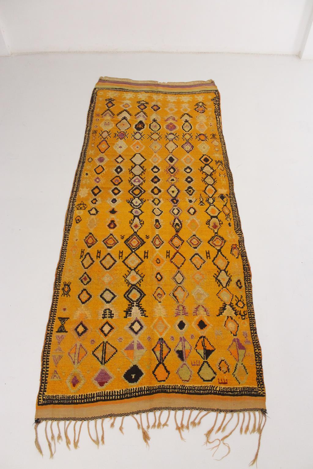 Dieser seltene Vintage-Teppich von Ait Ouaouzguite wurde in der Gegend von Taznakht, Marokko, hergestellt.

Es ist in einem leuchtenden Gelb - natürlich gefärbt mit Granatapfelschalen - mit schwarzen, violetten, magentafarbenen und orangefarbenen
