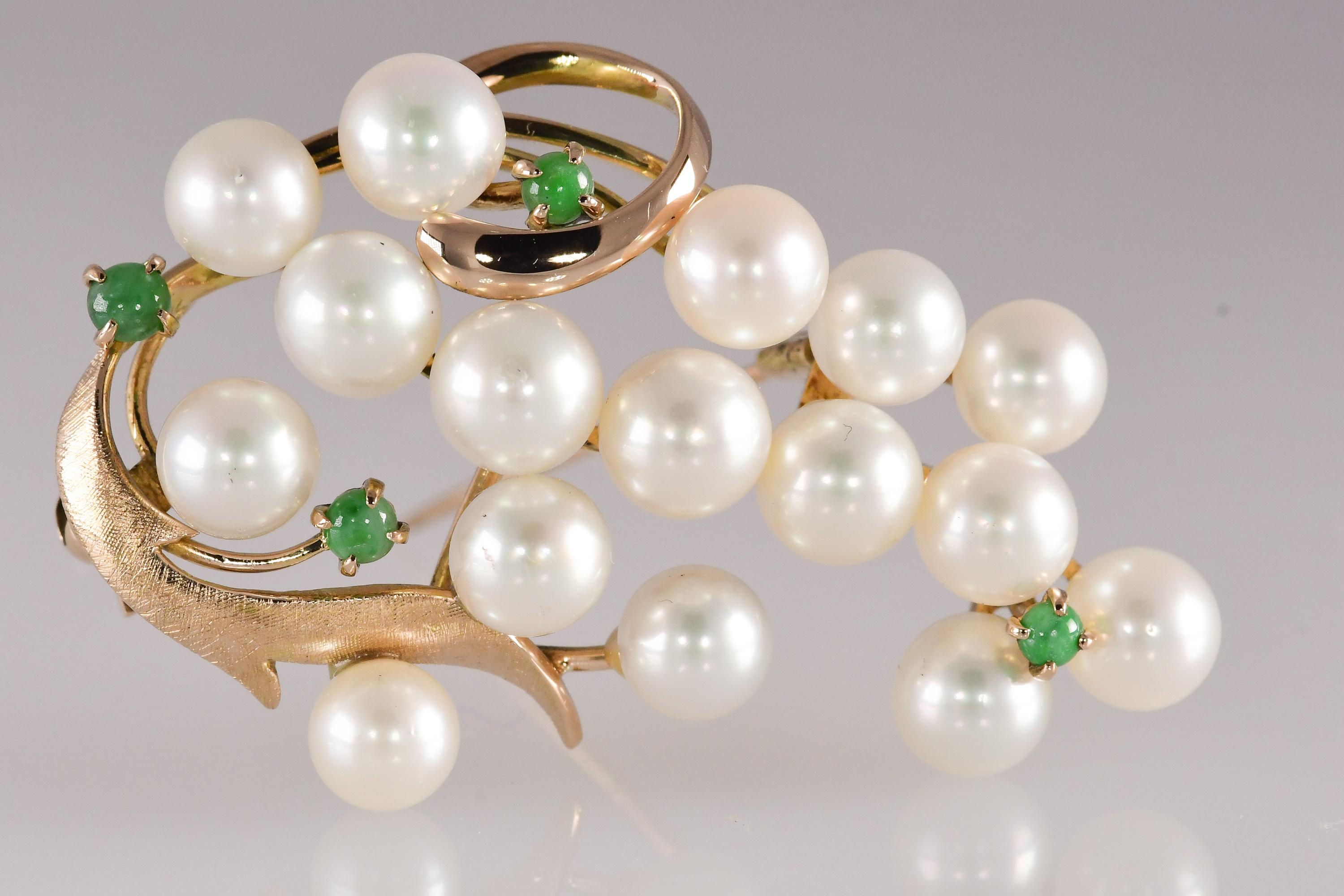 16 Akoya pearls with very high luster and no blemishing measure approximately 6 to 6 1/2 millimeters in diameter. Accenting the pearls are 4 round cabochon natural jadeite jade gemstones. The 14 karat yellow gold brooch measures approximately 1 7/8
