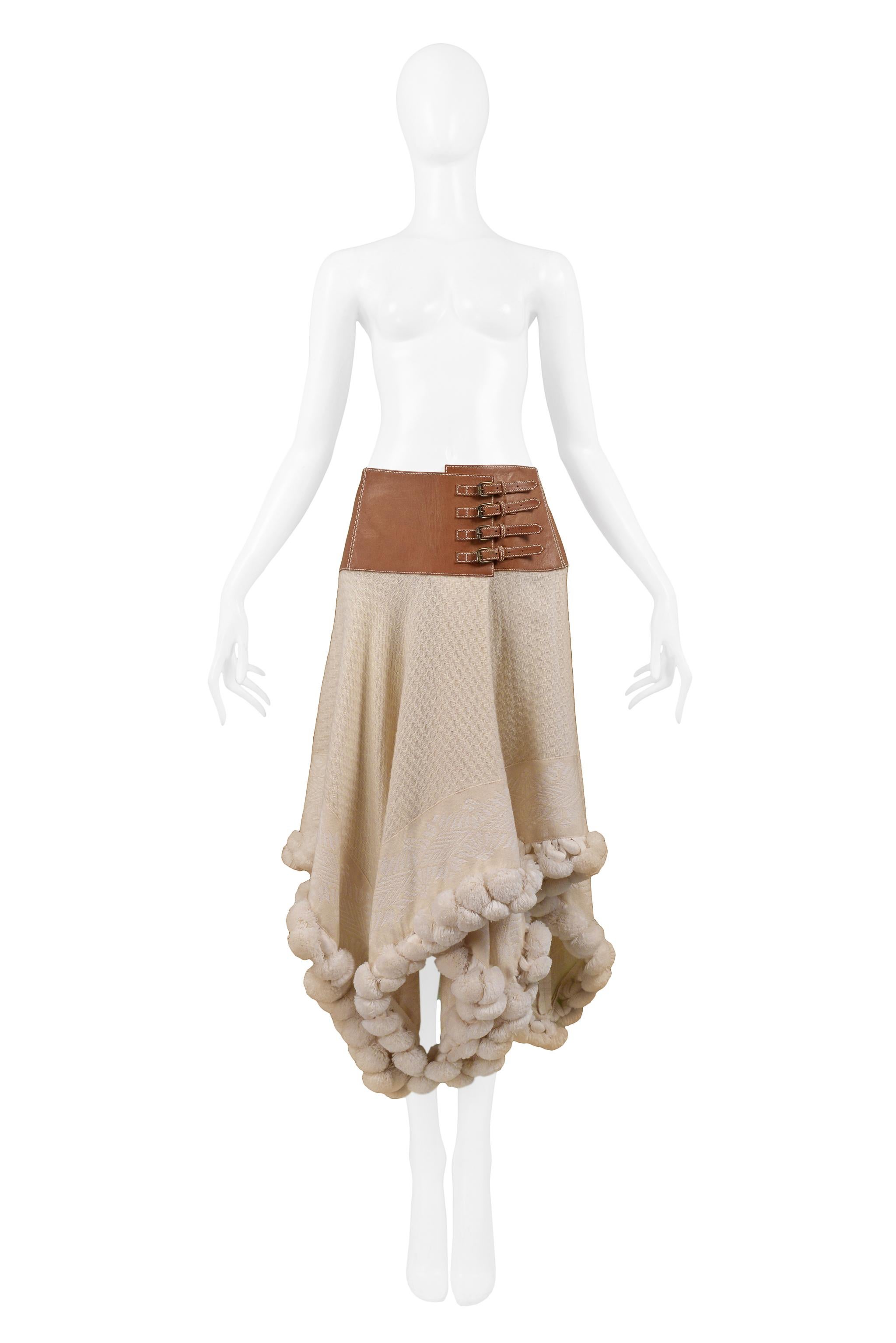 Vintage Alexander McQueen cream wool knit skirt featuring attached cognac brown leather belt with four buckles, oversized pom-poms at hem, and asymmetrical hemline. Collection 2003.

Excellent Vintage Condition

Size 42