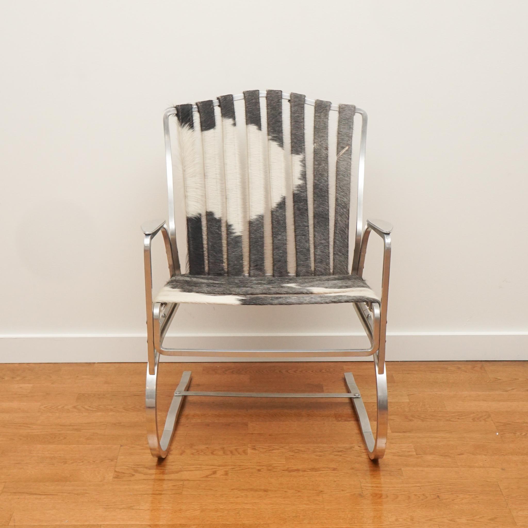 The aluminum armchair with cowhide straps, shown here, is from the 1950s. Despite its age the chair is in very good condition—from the aluminum frame to the cowhide straps which are original to the chair. If you're looking for some retro chic, this