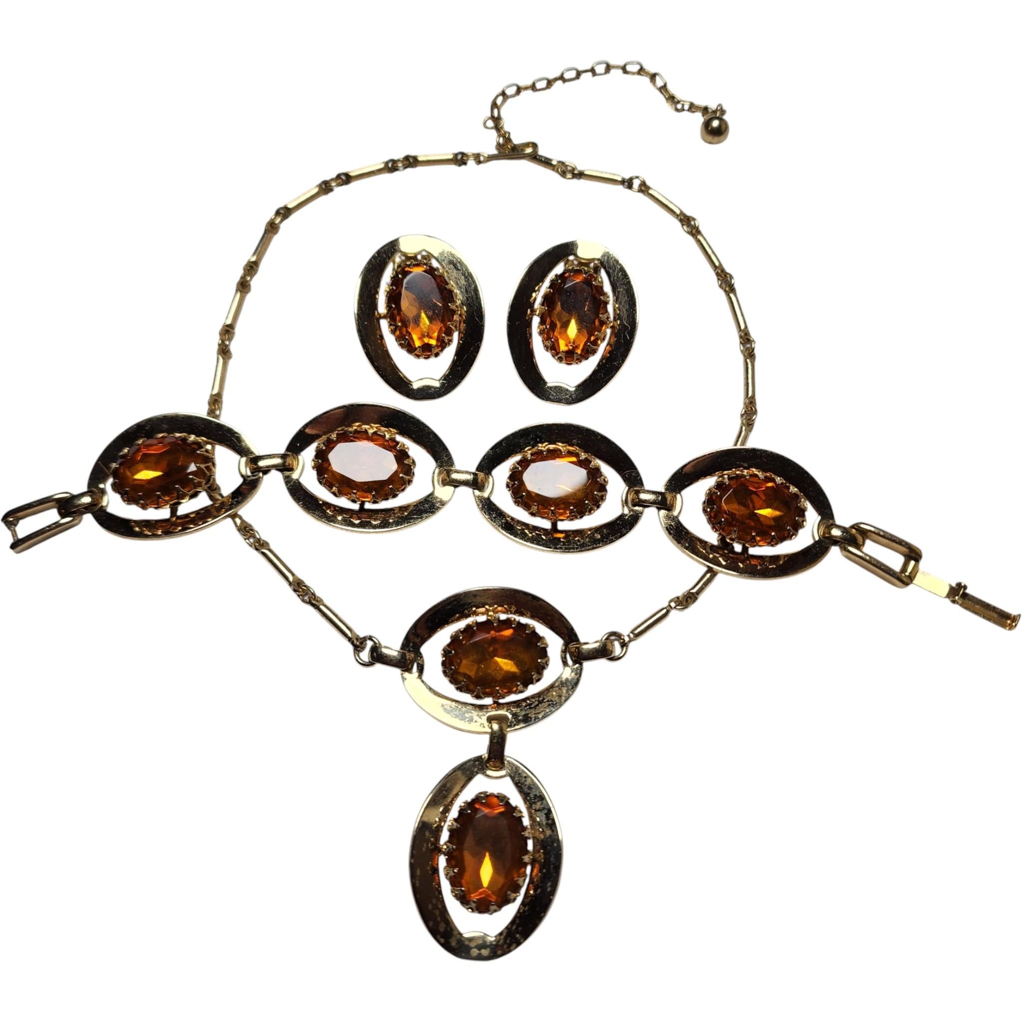 Parure vintage de 3 piezas de vidrio ámbar - collar, pulsera y pendientes, años 60
Descripción

Una espectacular parure de mediados de siglo con brillantes piedras facetadas de cristal ámbar engarzadas en esculturales marcos ovalados con textura en