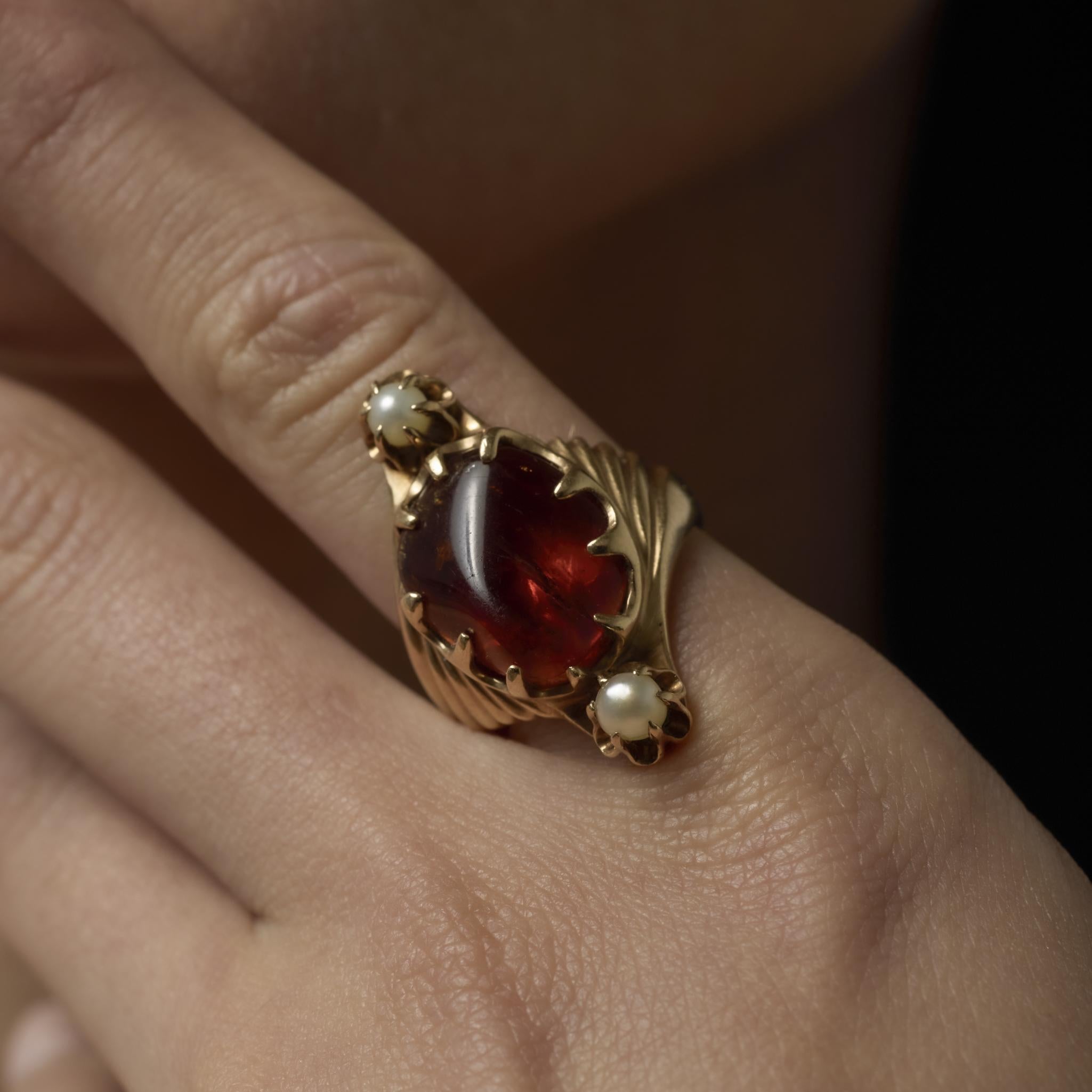 Un cálido anillo vintage de oro amarillo de 14k que muestra un cabujón de ámbar resplandeciente acentuado por dos perlas luminosas, creando un diseño distintivo y elegante.