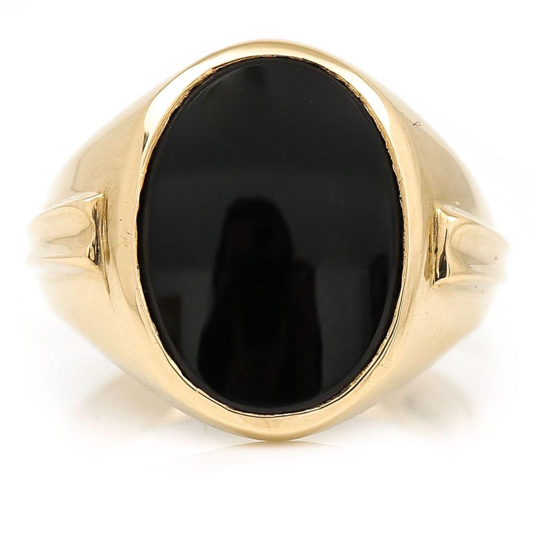 A large and impressive American vintage 10ct yellow gold oval onyx signet ring dating from the 1960s. The large ring with an oval polished onyx centre is set flush within the head of the piece. The shoulders are smartly decorated with raised
