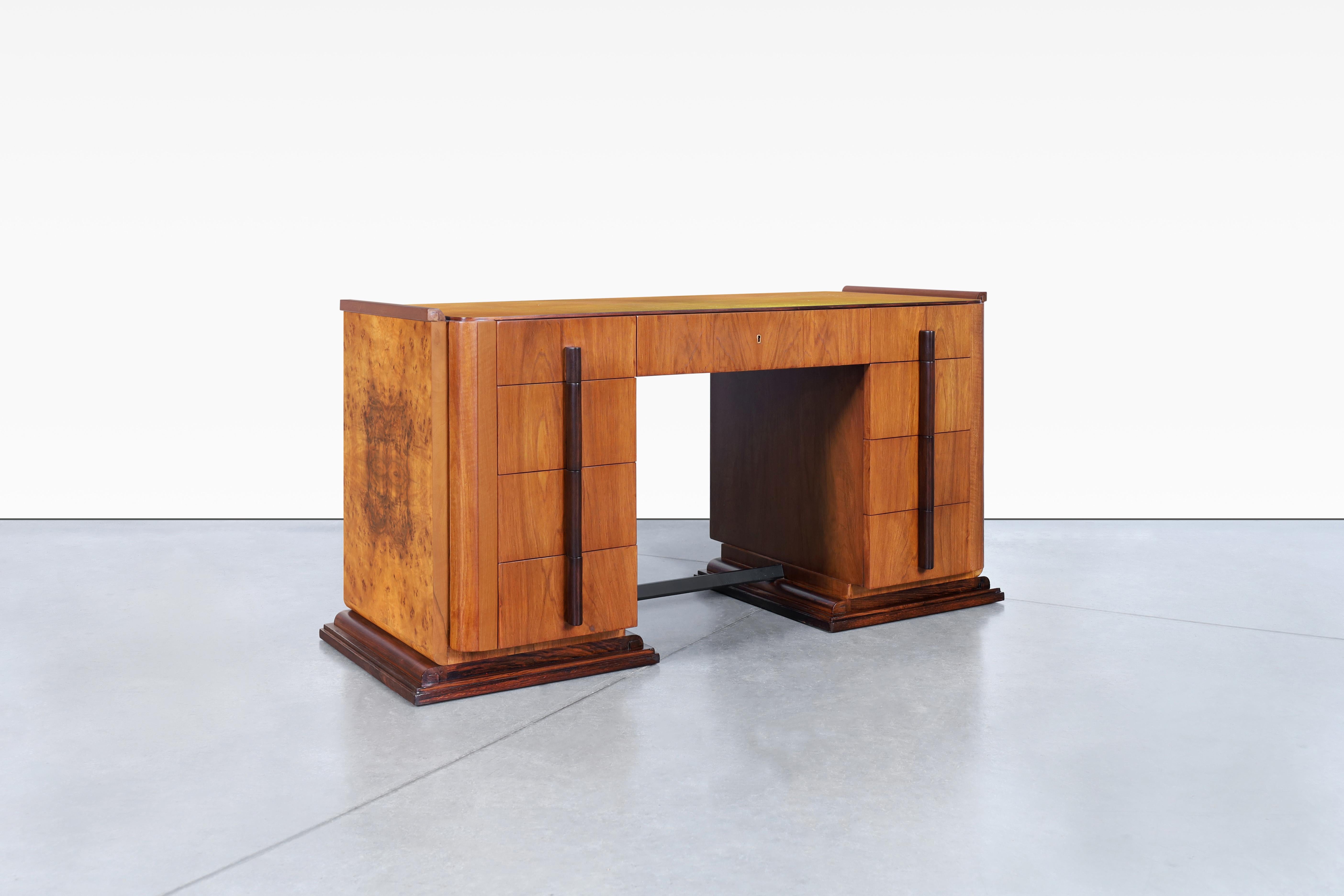 This vintage art deco desk from United States is a stunning piece from the 1930s. Its unique design features two shaped columns, each containing four pull-out drawers, as well as an additional drawer in the center. The front and back of the desk are