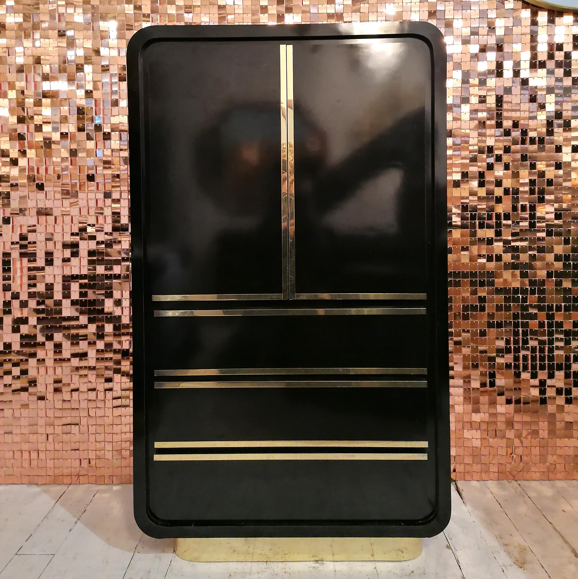 A stunning 1980s deco revival black laminate & gold tallboy / tall dresser. Waterfall ends, gold metal plinth base. Cabinet doors with shelf, below are 3 large drawers. 
Good vintage condition: a few very minor repaired chips, a little age-related