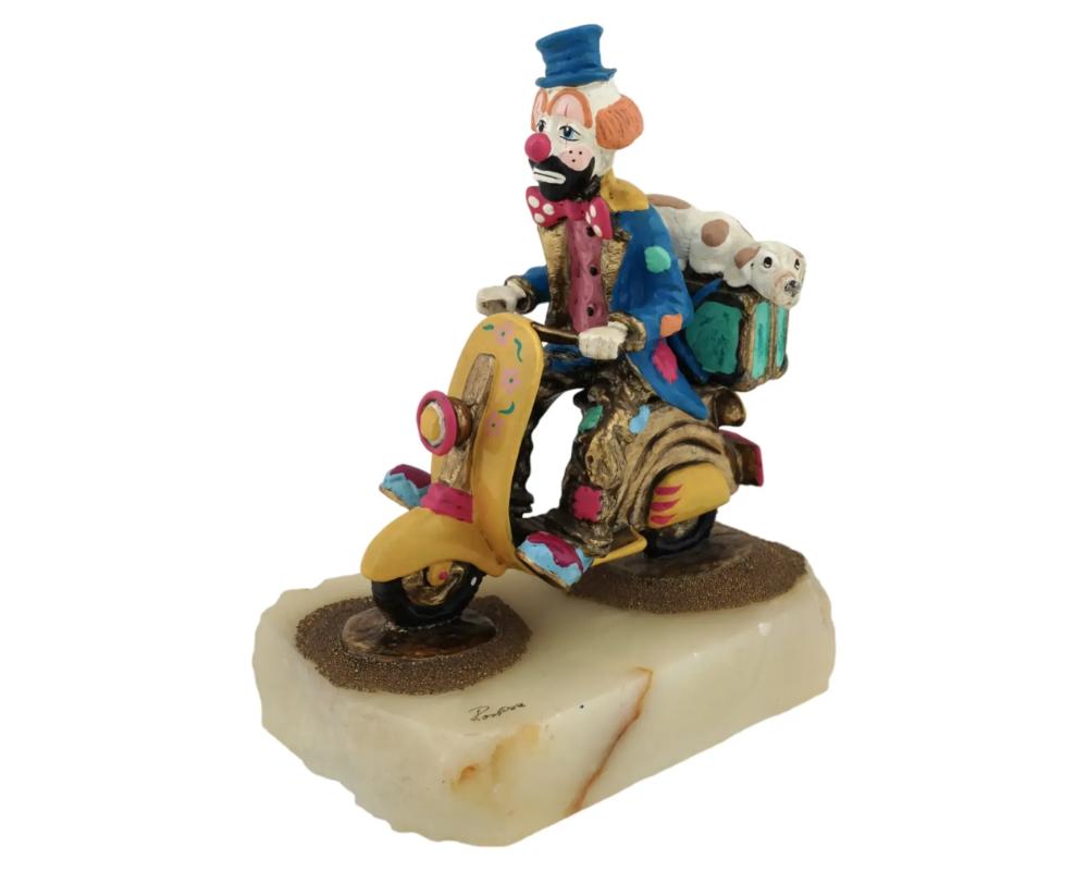 Figurita vintage de un payaso americano con un perro en Vespa, por Ron Lee, de 1947 a 2017. El payaso aparece con chaqueta y sombrero azules en una Vespa amarilla. Detrás del payaso, hay un perro tumbado sobre el equipaje. Firmado Ron y fechado en