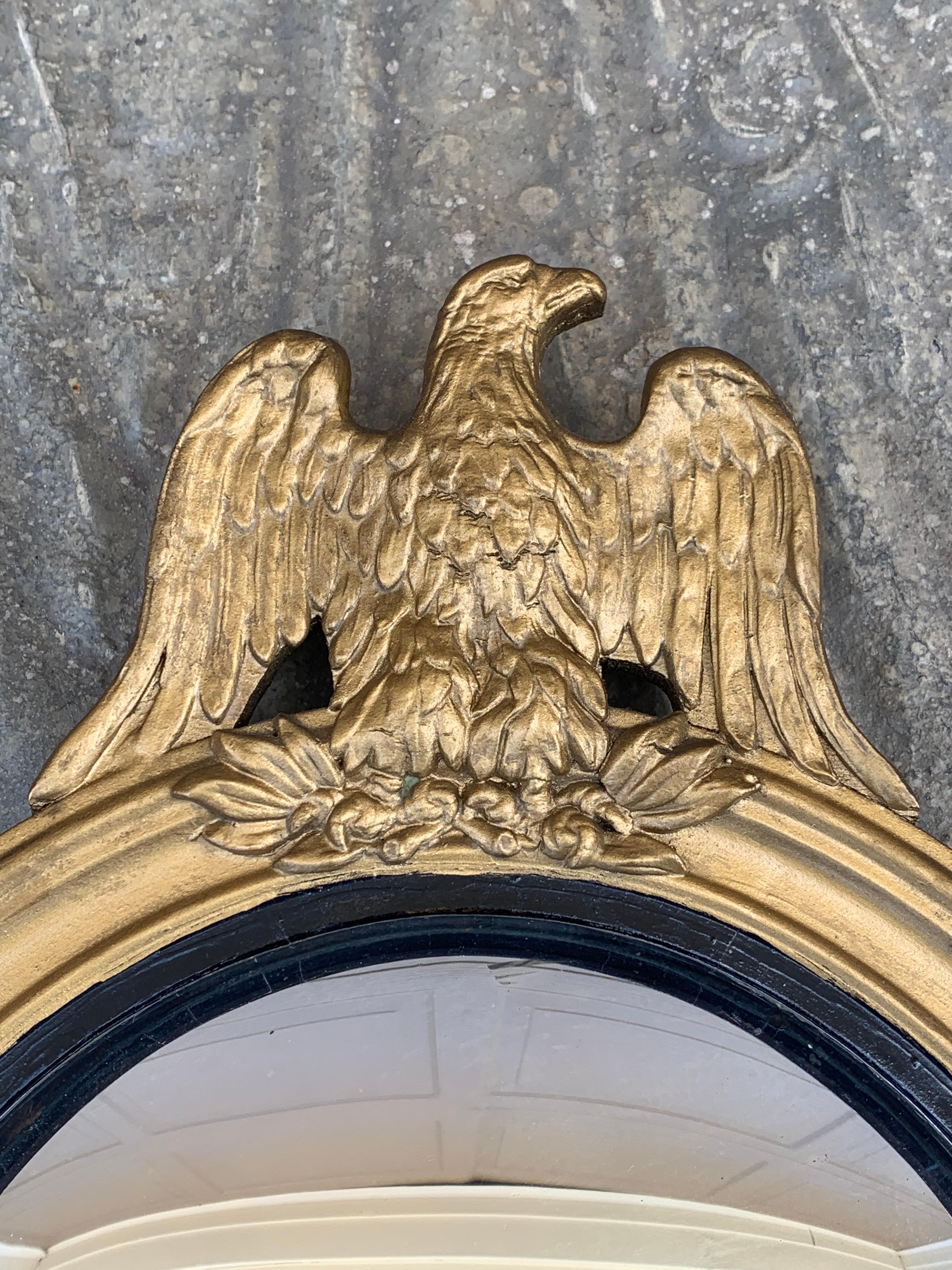 Magnifique miroir mural convexe à œil de bœuf de style Branch ou Regency, représentant un aigle sculpté aux ailes ouvertes, debout sur des branches d'olivier. 

États-Unis d'Amérique, milieu du XXe siècle

Cadre en bois doré, avec verre miroir