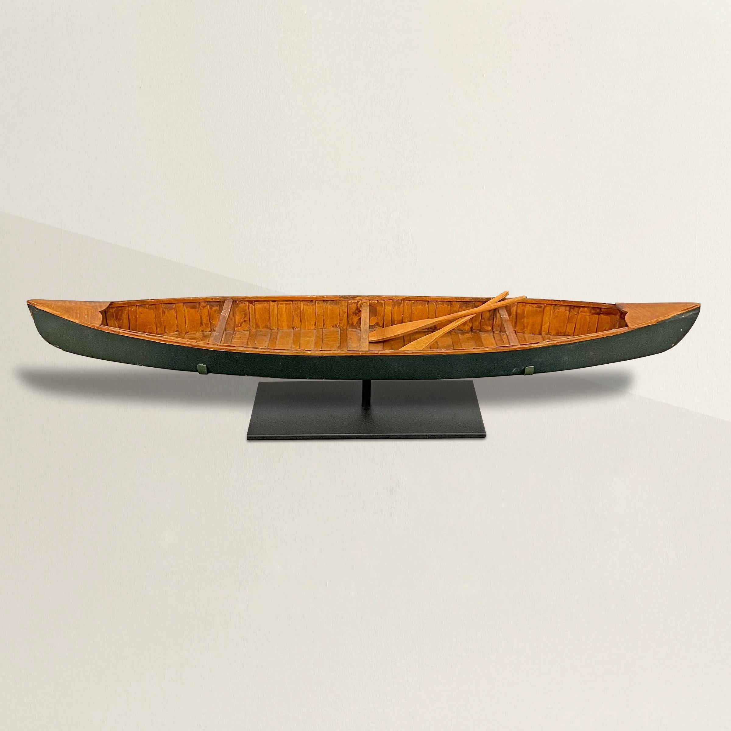 A whimsical mid-20th century American Folk Art hand built wooden canoe with removable oars, painted green, and mounted on a custom steel stand. The perfect gift for the outdoors person in your life!