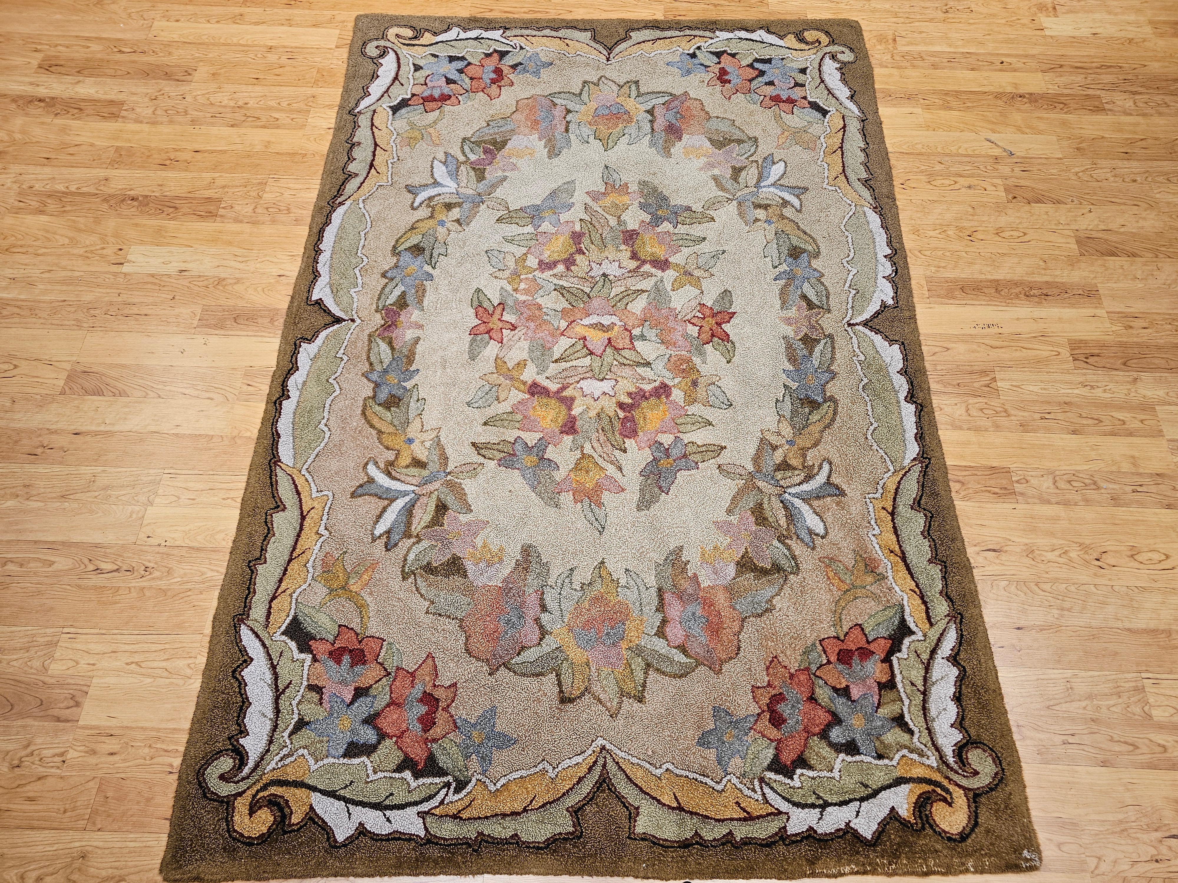 This exquisite vintage American hand-hooked rug, dating from the early 20th century, features a charming large-scale floral pattern rendered in a soft, nature-inspired color palette. Shades of green, blue, red, pink, purple, and hints of golden