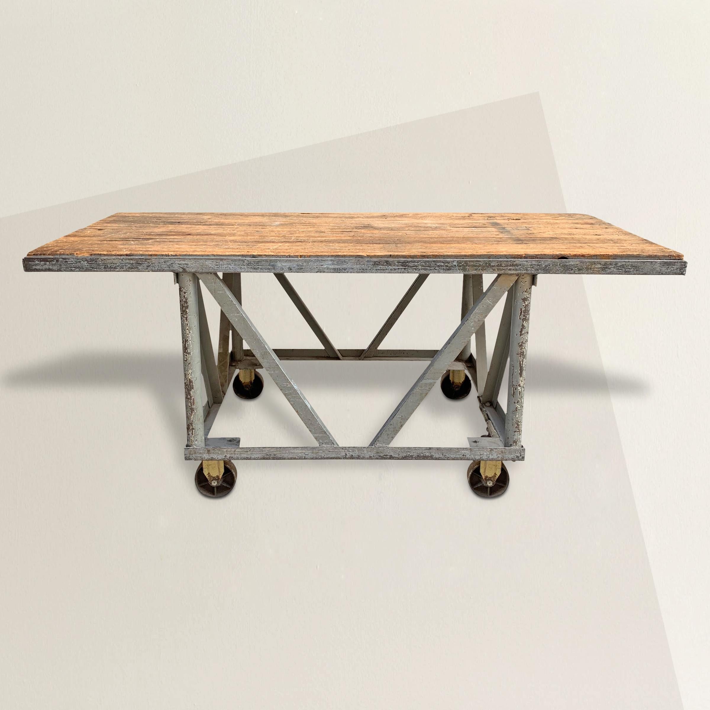 An incredible early 20th century American industrial steel table with a plank wood top with a well-worn surface. A locking mechanism on one side can be engaged to keep the table stationary, or disengaged so it can moved around. This would be the
