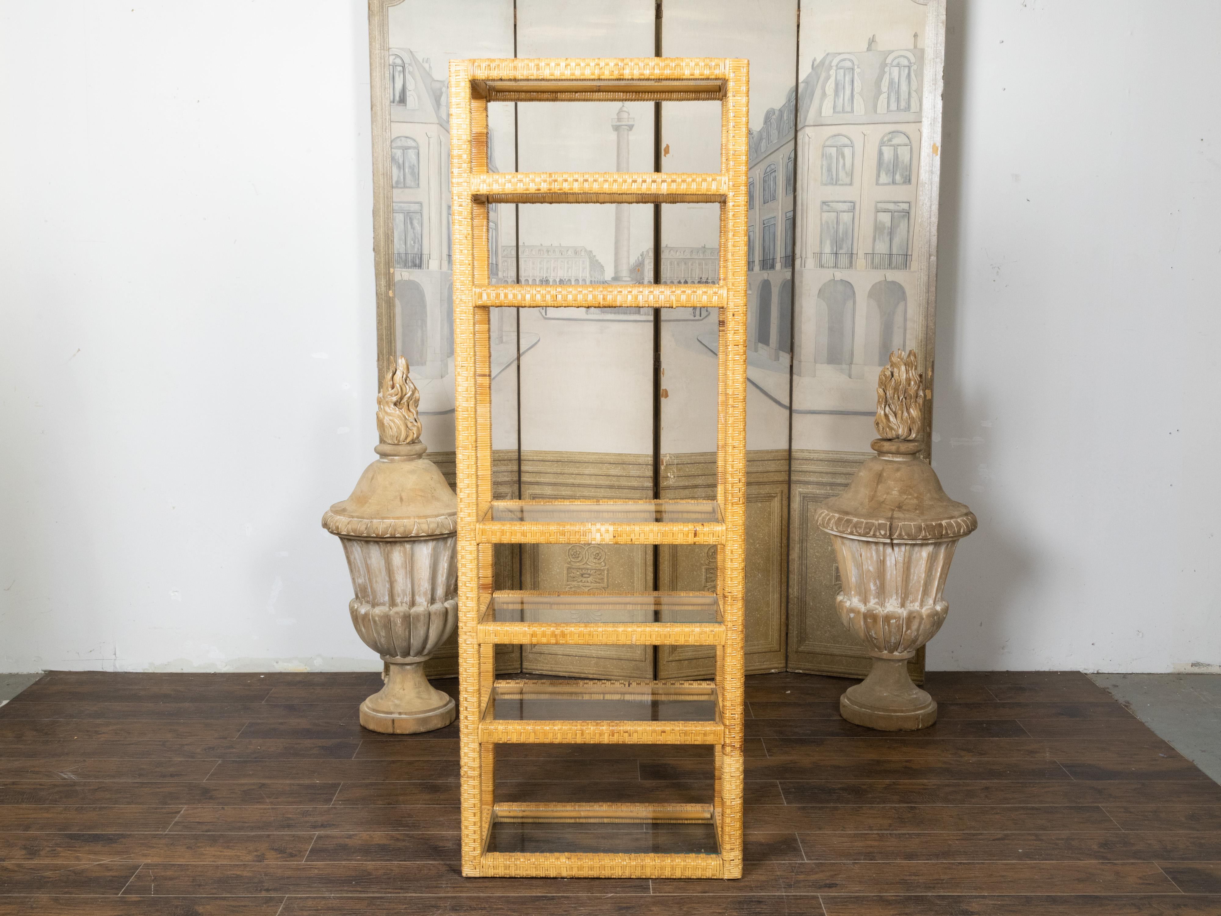 An American rattan étagère from the mid 20th century period, with linear silhouette and glass shelves. Made in the USA during the midcentury period, this étagère charms us with its simple lines and rustic appearance. The piece showcases a rattan